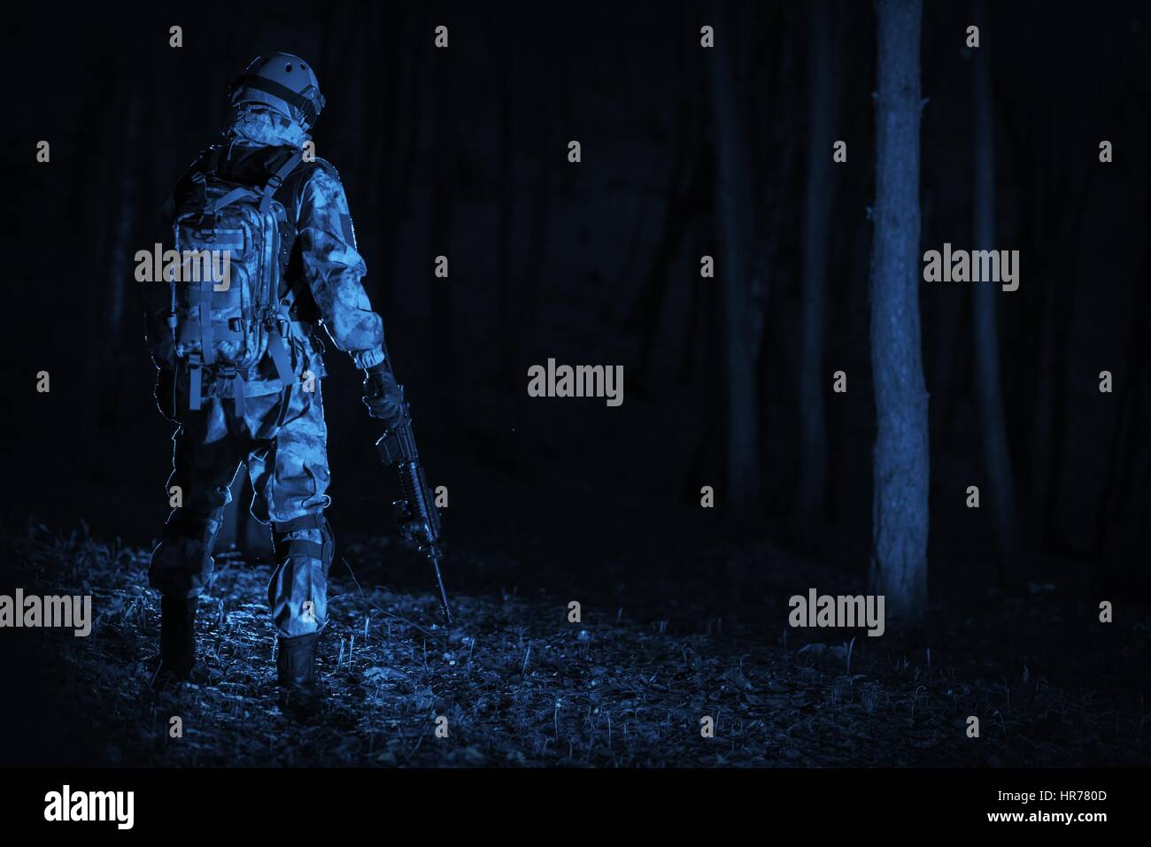 Operazione militare di notte. Colore blu scuro Concetto di classificazione. Soldato con il fucile di stare indietro a metà del passo foresta scura. Foto Stock