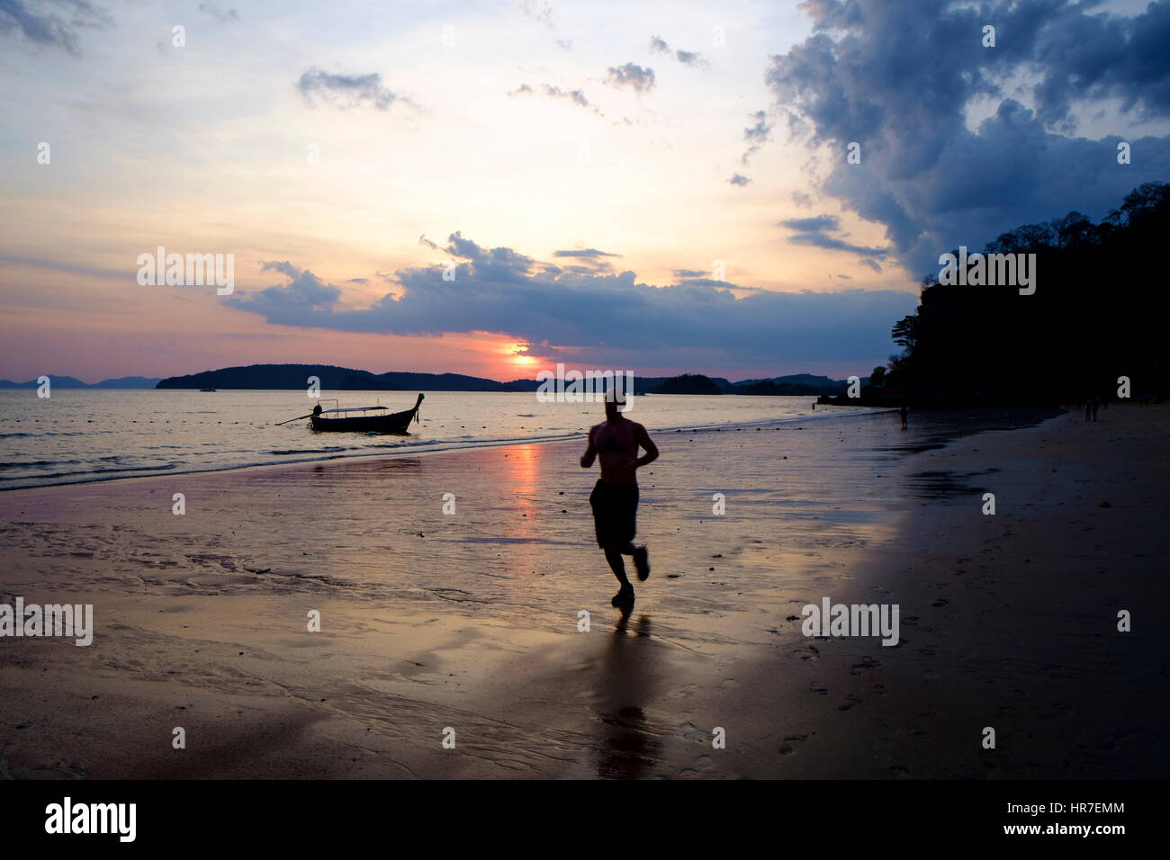 Un uomo che corre sulla Spiaggia Ao Nang al tramonto, Provincia di Krabi, Thailandia. Foto Stock