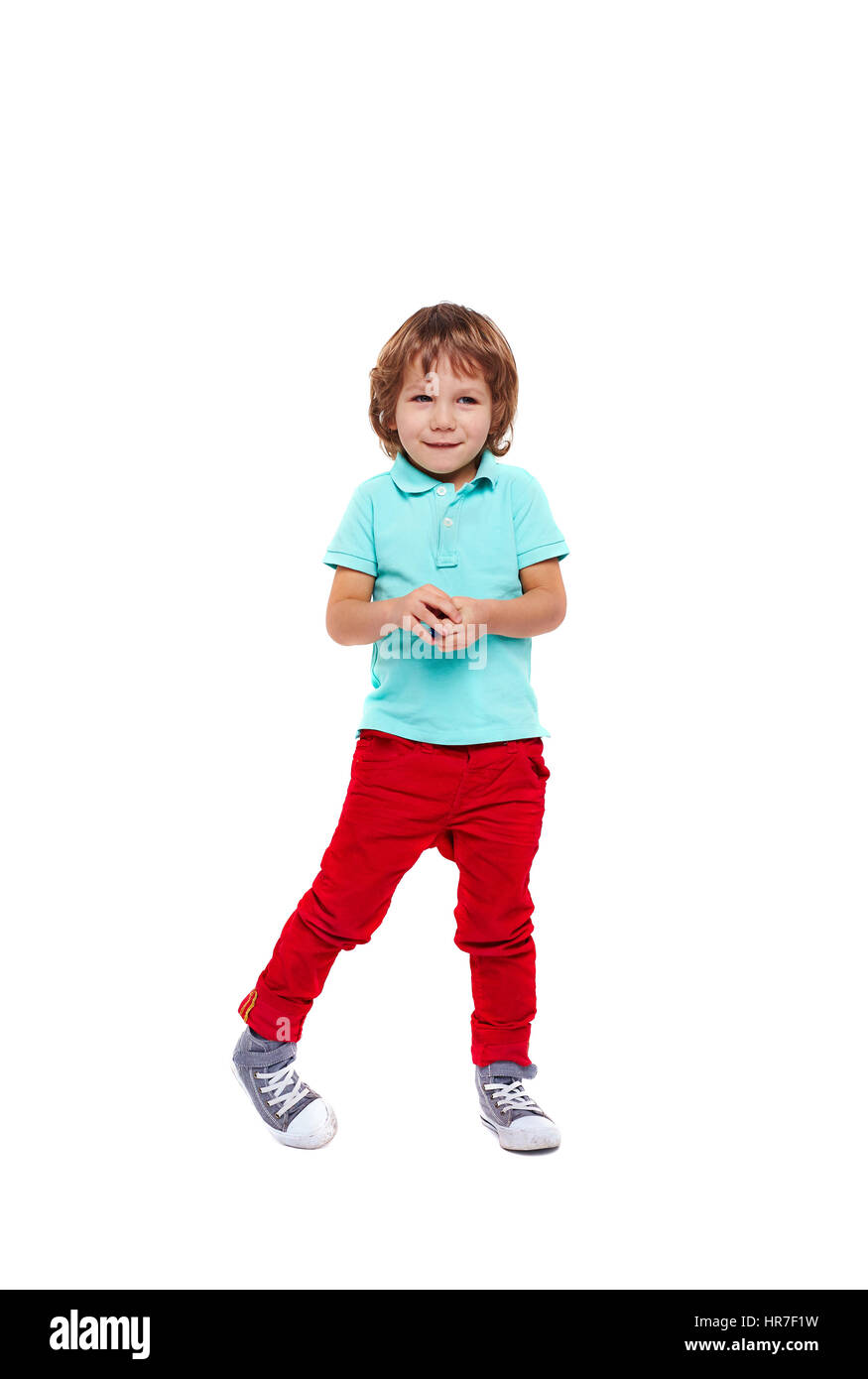 Corpo pieno ritratto di timido bambino vestito in bright abiti colorati sogghignando permanente e in posa goffamente contro uno sfondo bianco Foto Stock