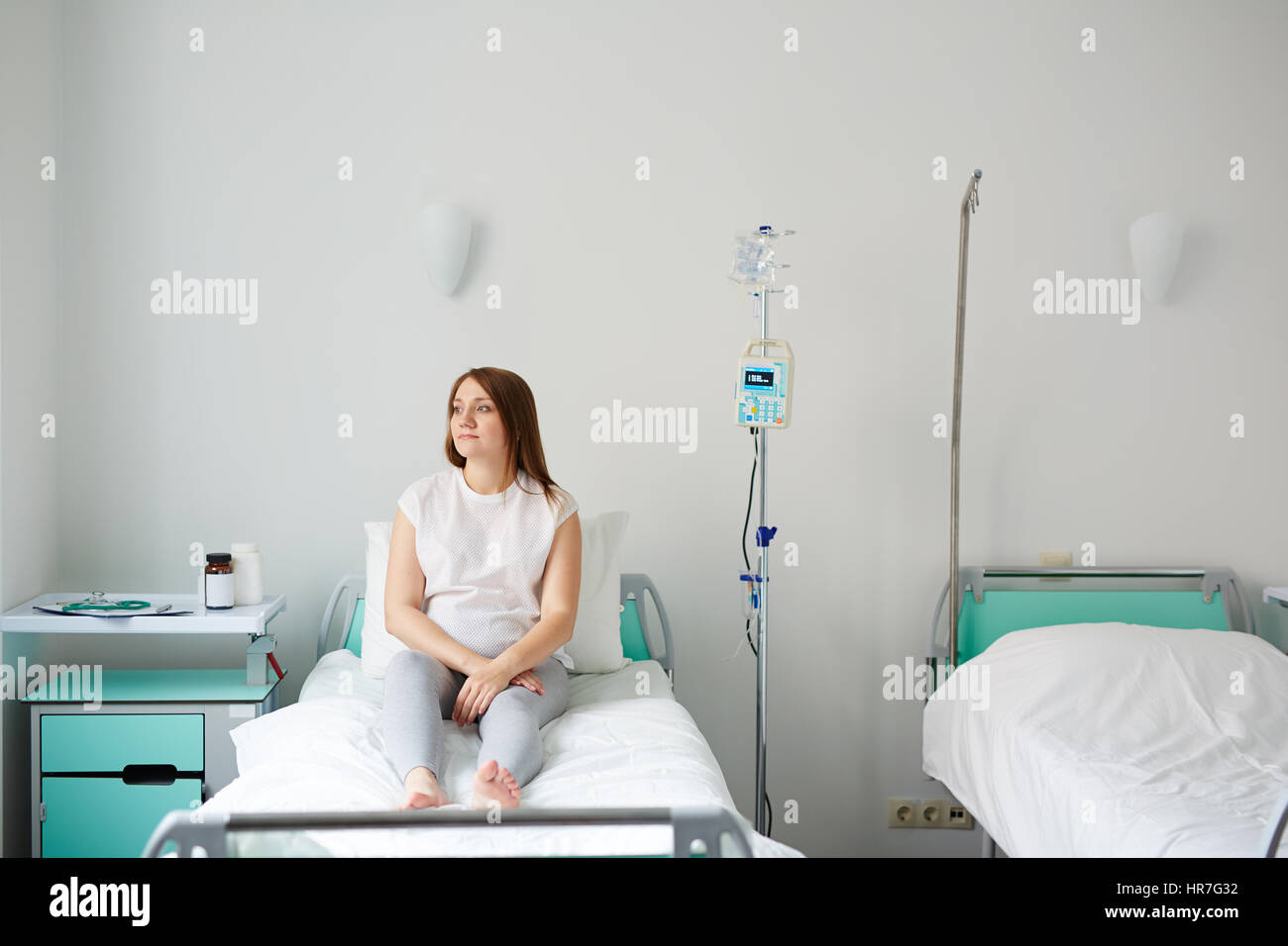 Donna incinta sdraiato sul letto nella stanza di ospedale e guardando al lato premurosamente Foto Stock