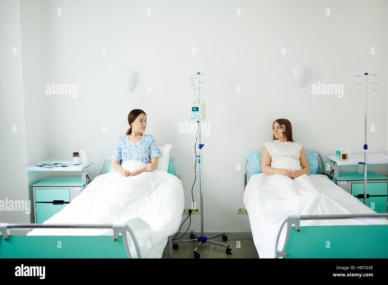 Due donne in stato di gravidanza in appoggio in letti nella stanza di ospedale e parlare dei bambini educazione Foto Stock