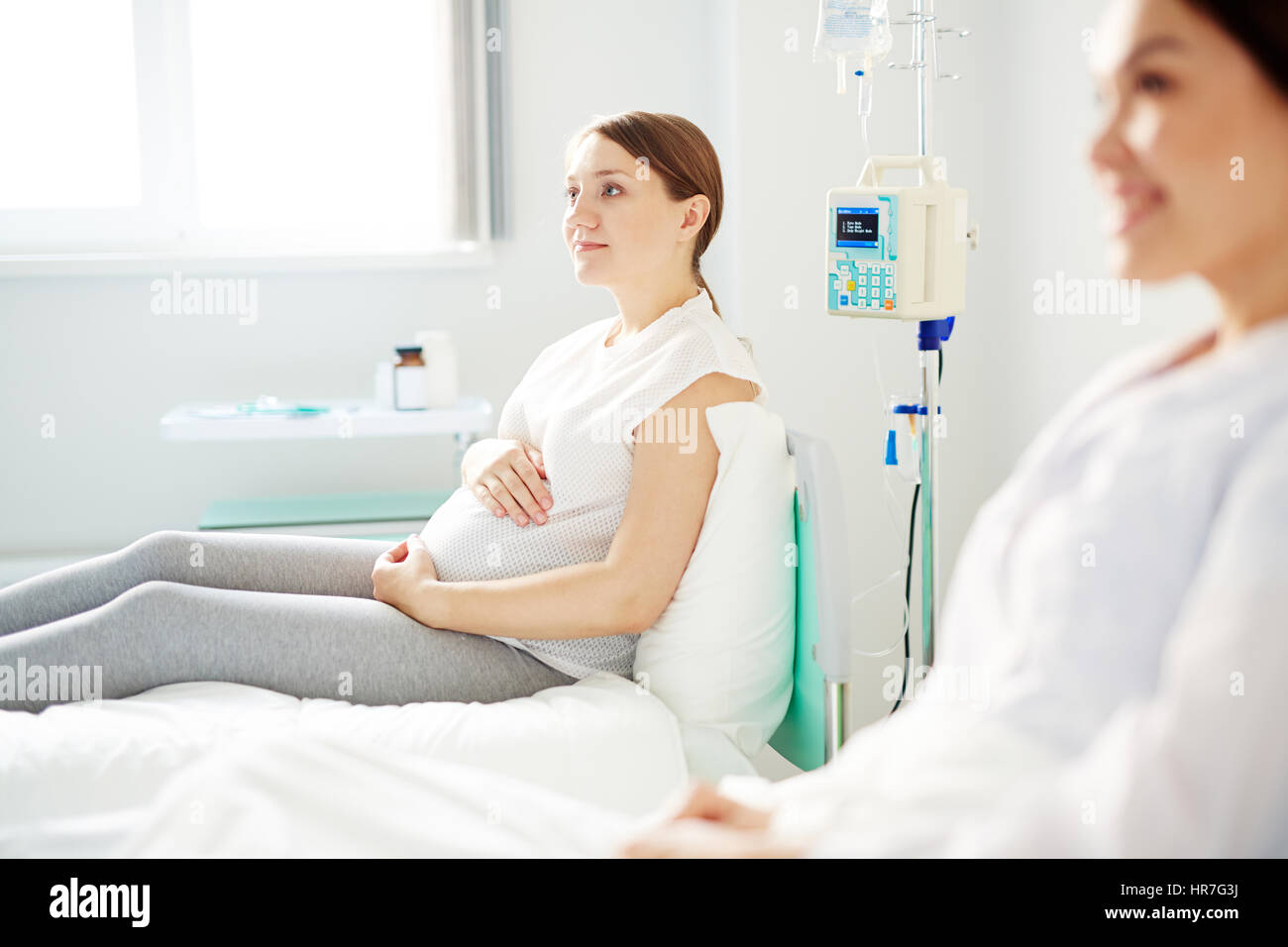 Vista laterale della donna incinta in appoggio nella stanza di ospedale e pensando a nome per il suo prossimo baby Foto Stock