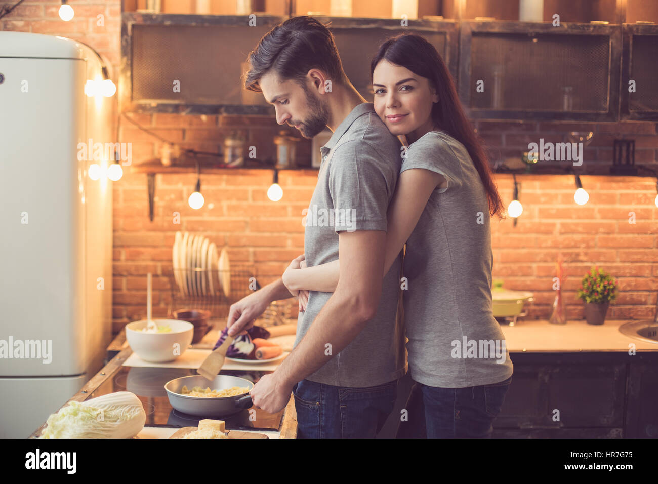 Giovane bella giovane in cucina. Famiglia di due nella preparazione degli alimenti. Donna che guarda la fotocamera e abbracciando uomo mentre egli rendendo deliziosi piatti di pasta. Un grazioso soppalco in Foto Stock