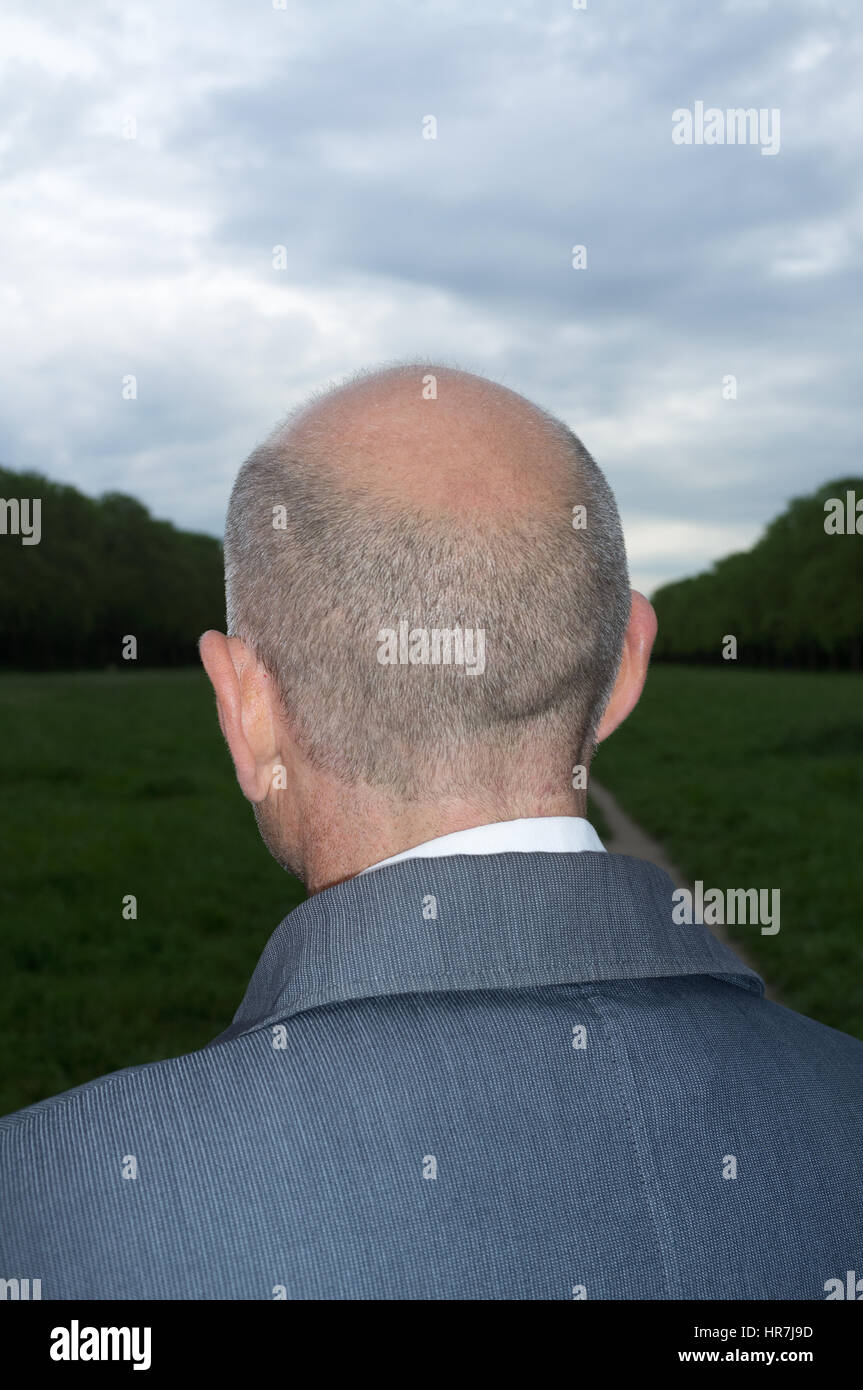 Vista posteriore del ritratto di un calvo uomo di mezza età guardando lontano nel bosco Foto Stock