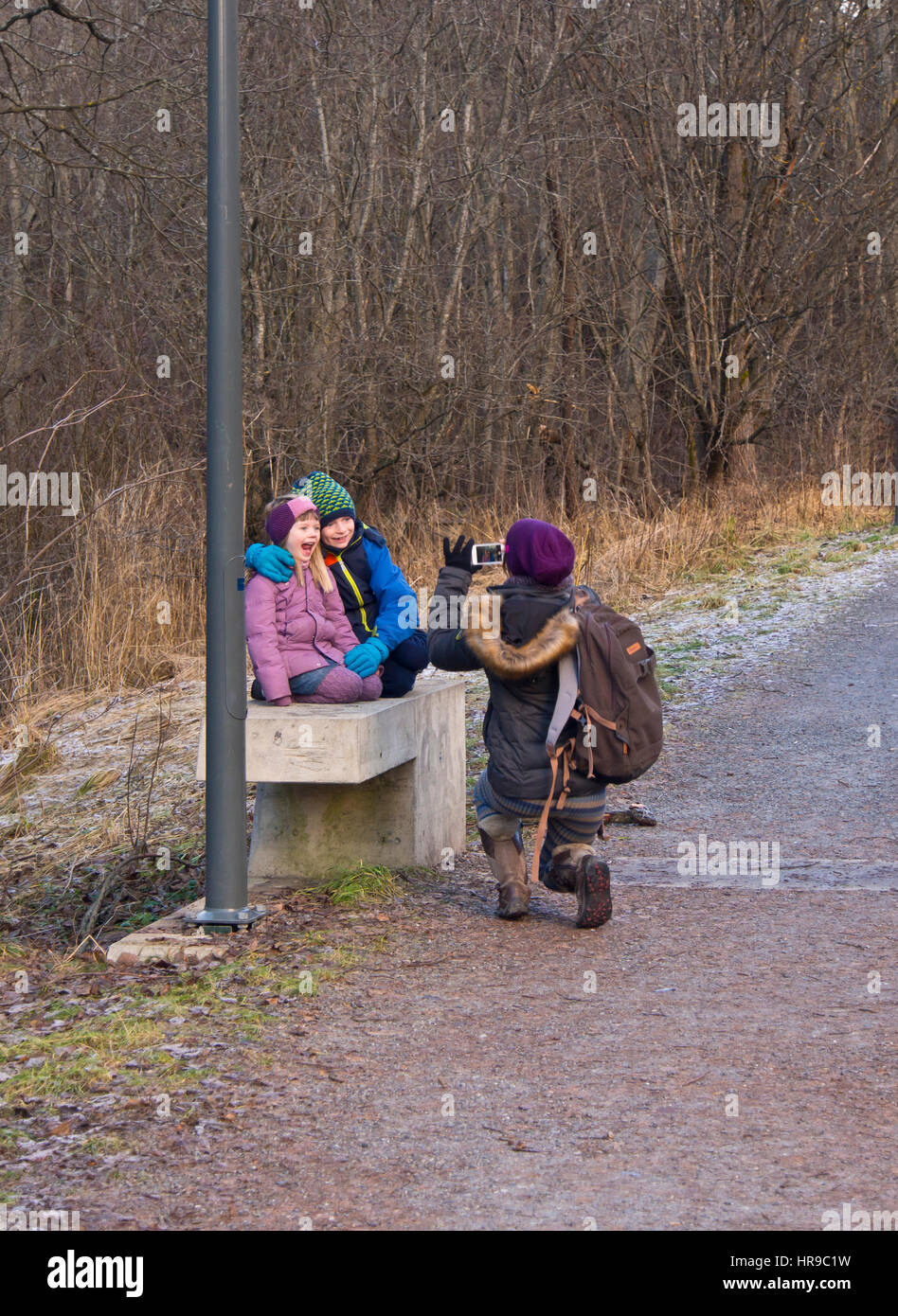 Fotografia dello smartphone, madre su una gita domenicale riprese due bambini rendendo volti e ridere su un banco in una foresta, Oslo Norvegia Foto Stock