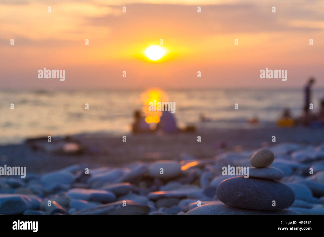 Un giovane e ripiegati a piramide Zen pietre ghiaia sul mare spiaggia al tramonto Foto Stock