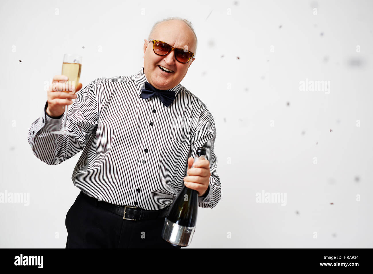 Ritratto di elegante uomo anziano in camicia a righe con il filtro bow tie tenendo un bicchiere di champagne, rendendo un toast e sorridente felicemente Foto Stock