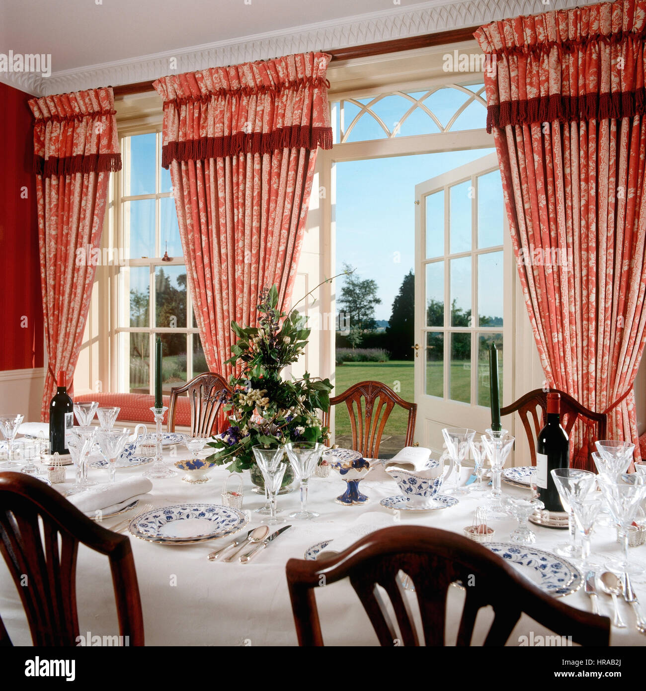 Cina e vetreria in sala da pranzo rosso con tende a motivi geometrici inquadrature spettacolari viste sul giardino Foto Stock