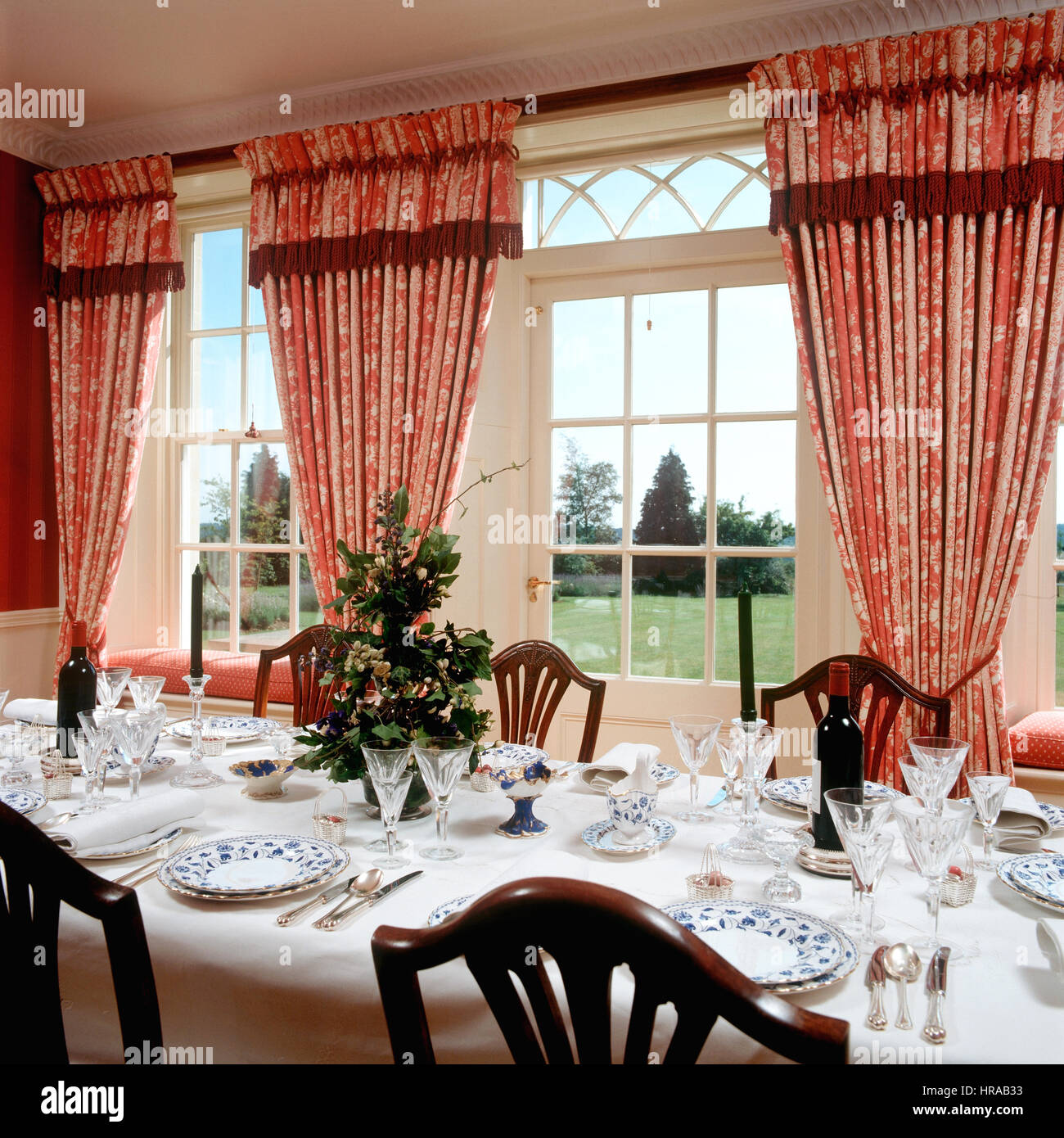 Cina e vetreria in sala da pranzo rosso con tende a motivi geometrici e spettacolare vista sul giardino Foto Stock