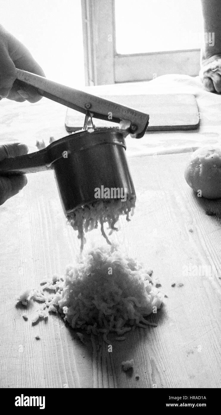 Mani con un ricer di patate, preparando gnocchi di patate in una cucina rustica con luce naturale del sole Foto Stock