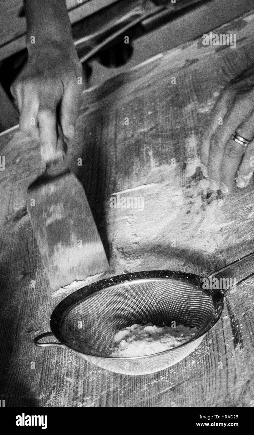 Close up della casalinga di raschiatura la farina in eccesso in un crivello di pulizia worksurface Foto Stock