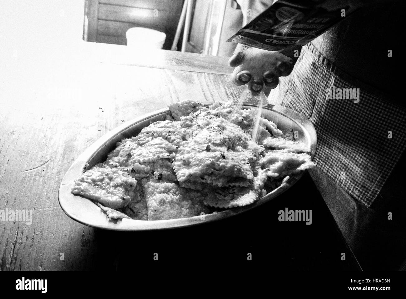 Mani cospargere il formaggio grattugiato su ravioli fatti in casa Foto Stock
