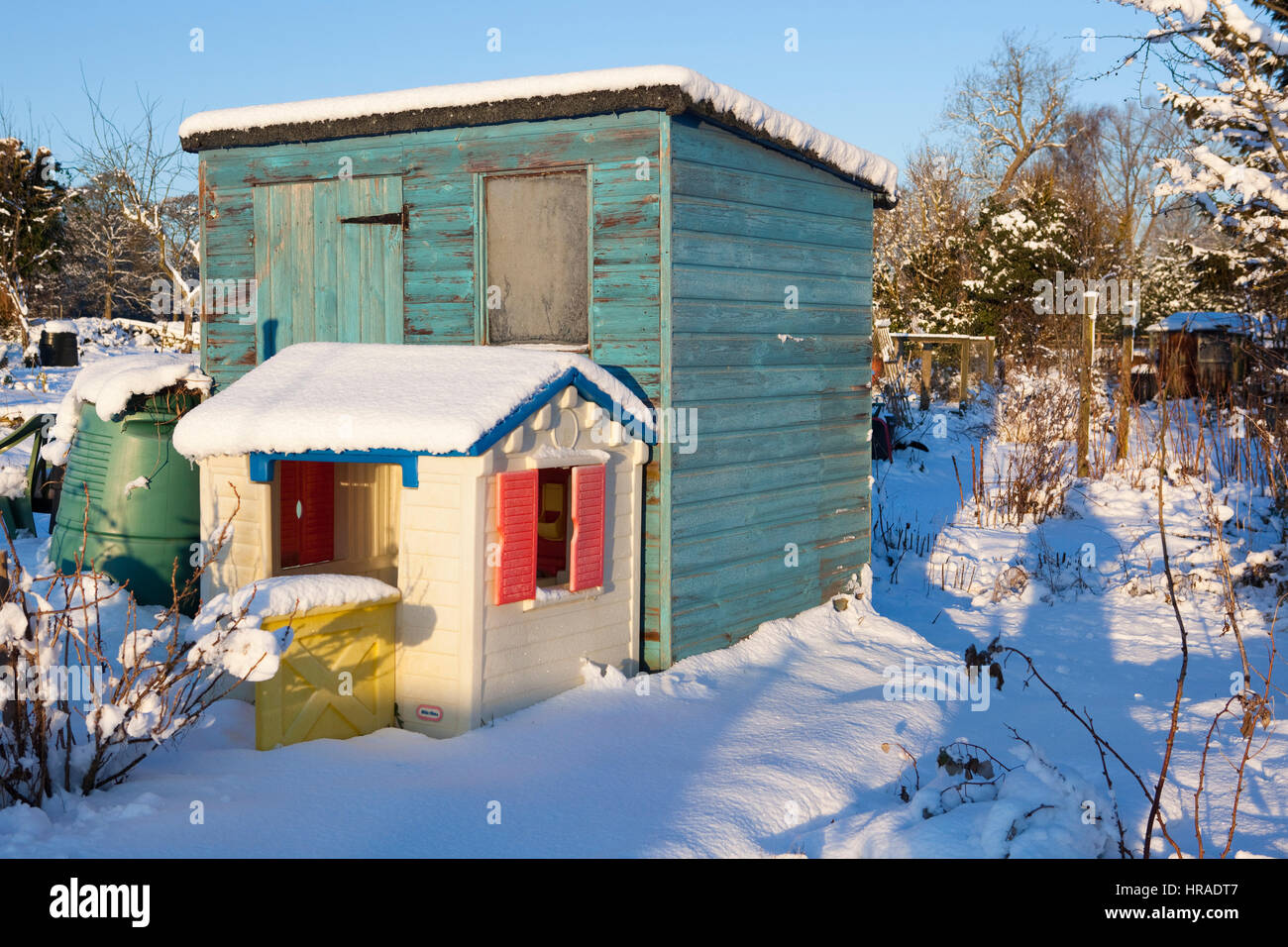 Un dipinto di verde sparso sorge su un lotto di terreno ricoperto di neve con un gioco da ragazzi il mirroring della casa è anche coperto di neve su un luminoso giorno inverni. Foto Stock