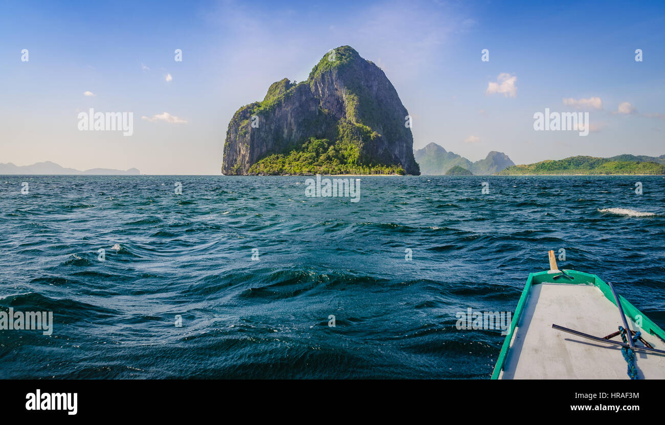 Banca barca si avvicina enorme isola rocciosa sulla giornata di vento, El, Nido, PALAWAN FILIPPINE Foto Stock