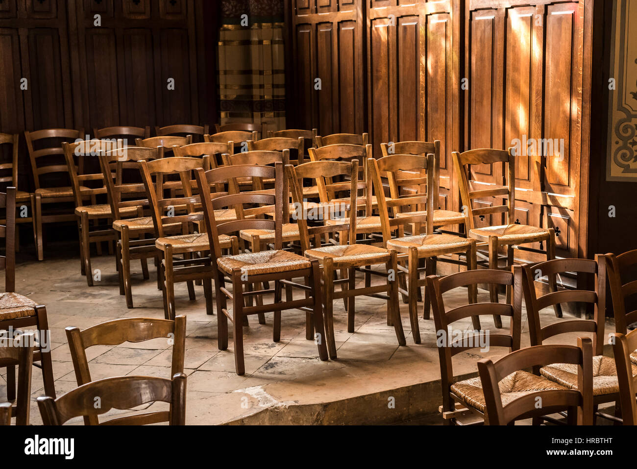 Sedie di legno con tessuto sedili in vimini sono illuminate dal sole in una chiesa di Parigi, Francia. Foto Stock