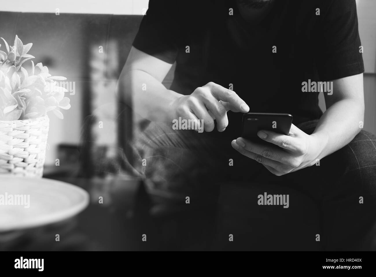 Designer man mano utilizzando smart phon per i pagamenti mobili shopping online,omni canale,seduto sul divano nel soggiorno,vaso rattan con impianti e t in legno Foto Stock