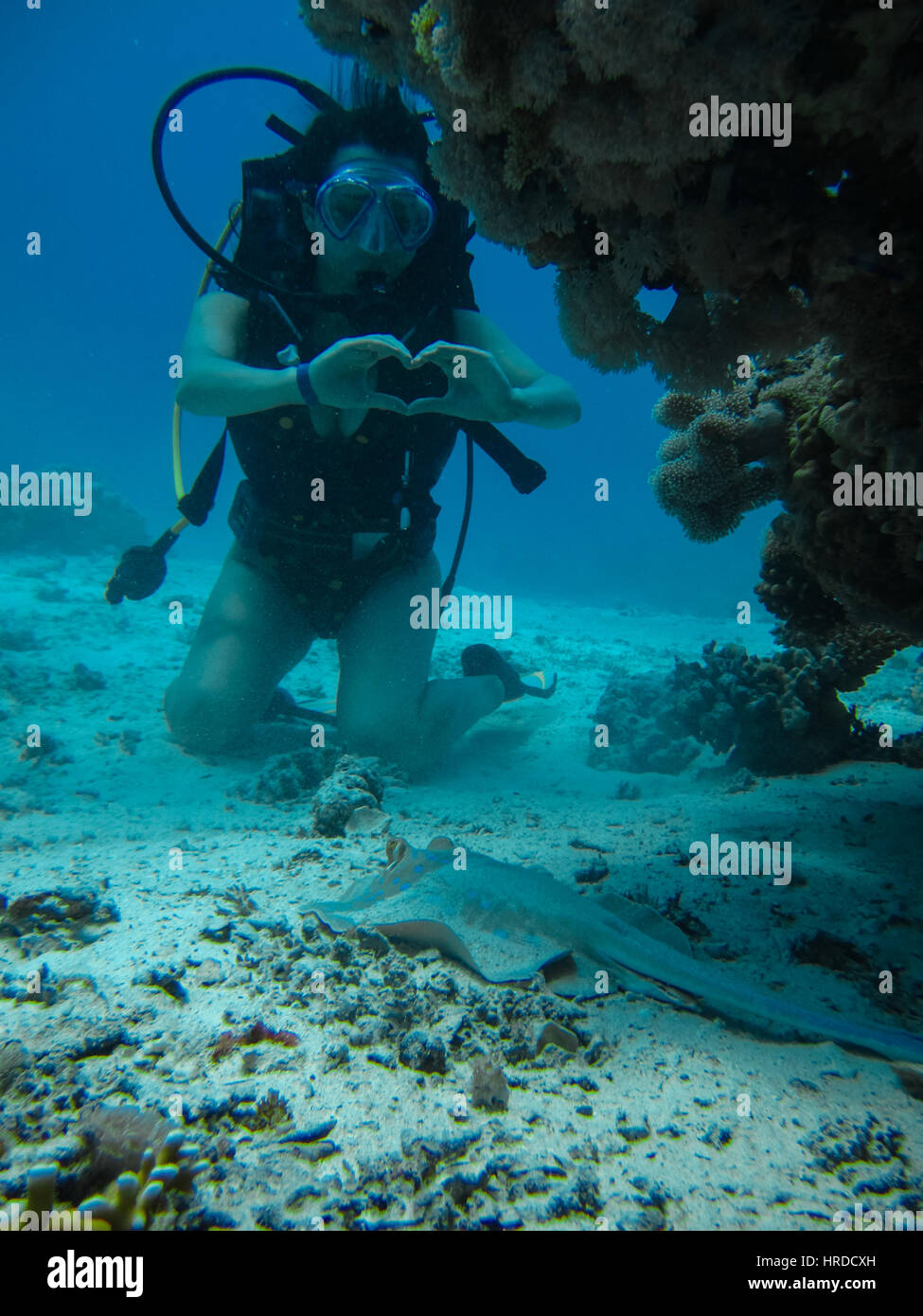 Giovane donna sul fondo marino che mostra il segnale di amore per una piccola pendenza mentre le immersioni con scuba Foto Stock