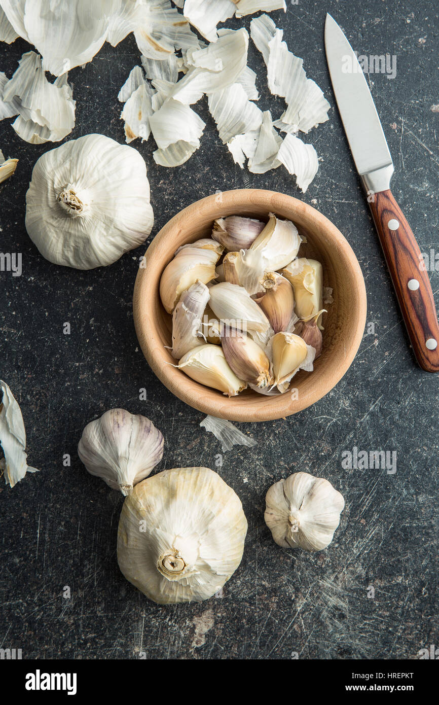 Aglio fresco nella ciotola di legno con il coltello. Vista dall'alto. Foto Stock