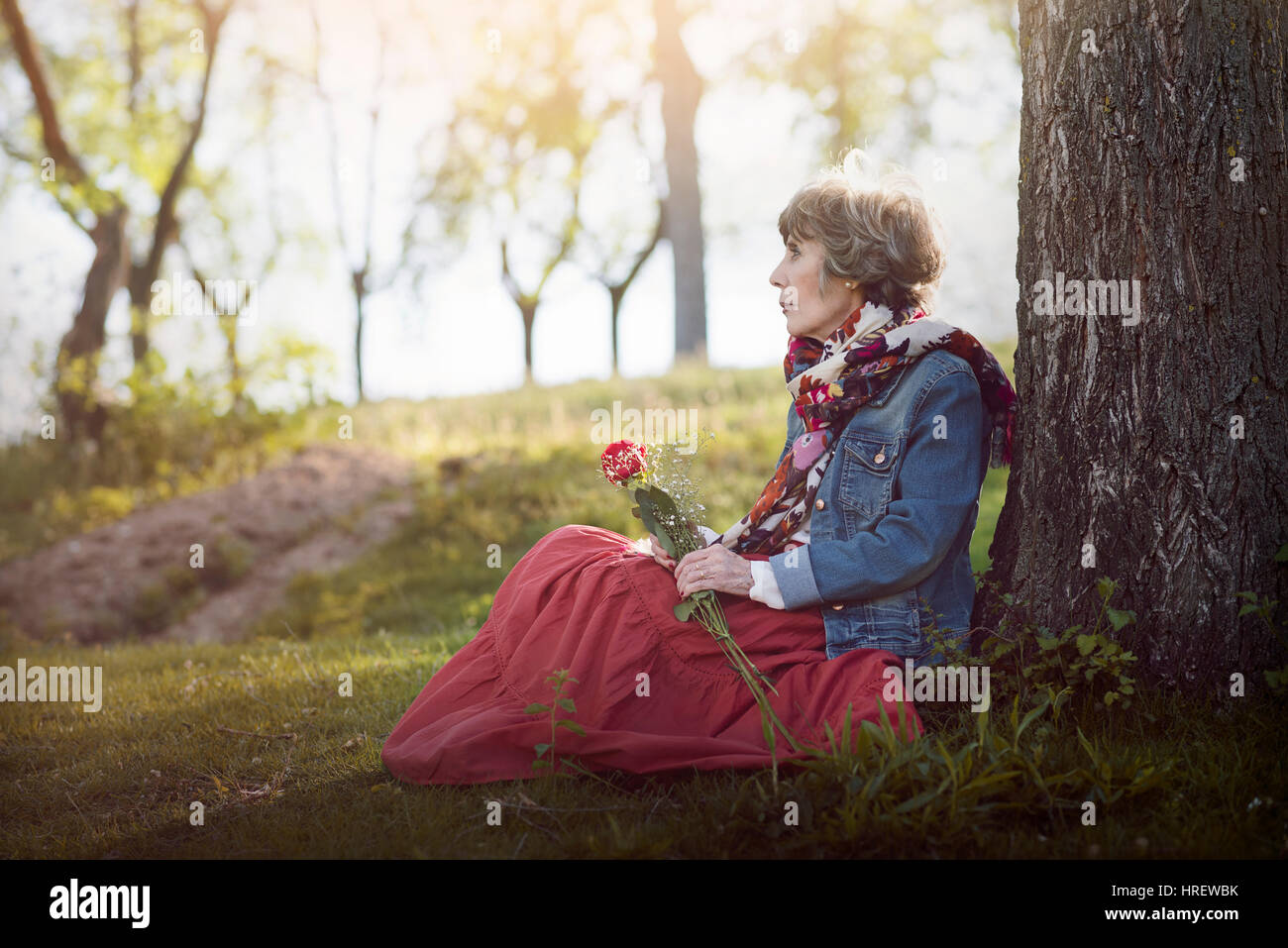 Malinconici senior donna seduta sull'erba. senior donna con una rosa in mano Foto Stock