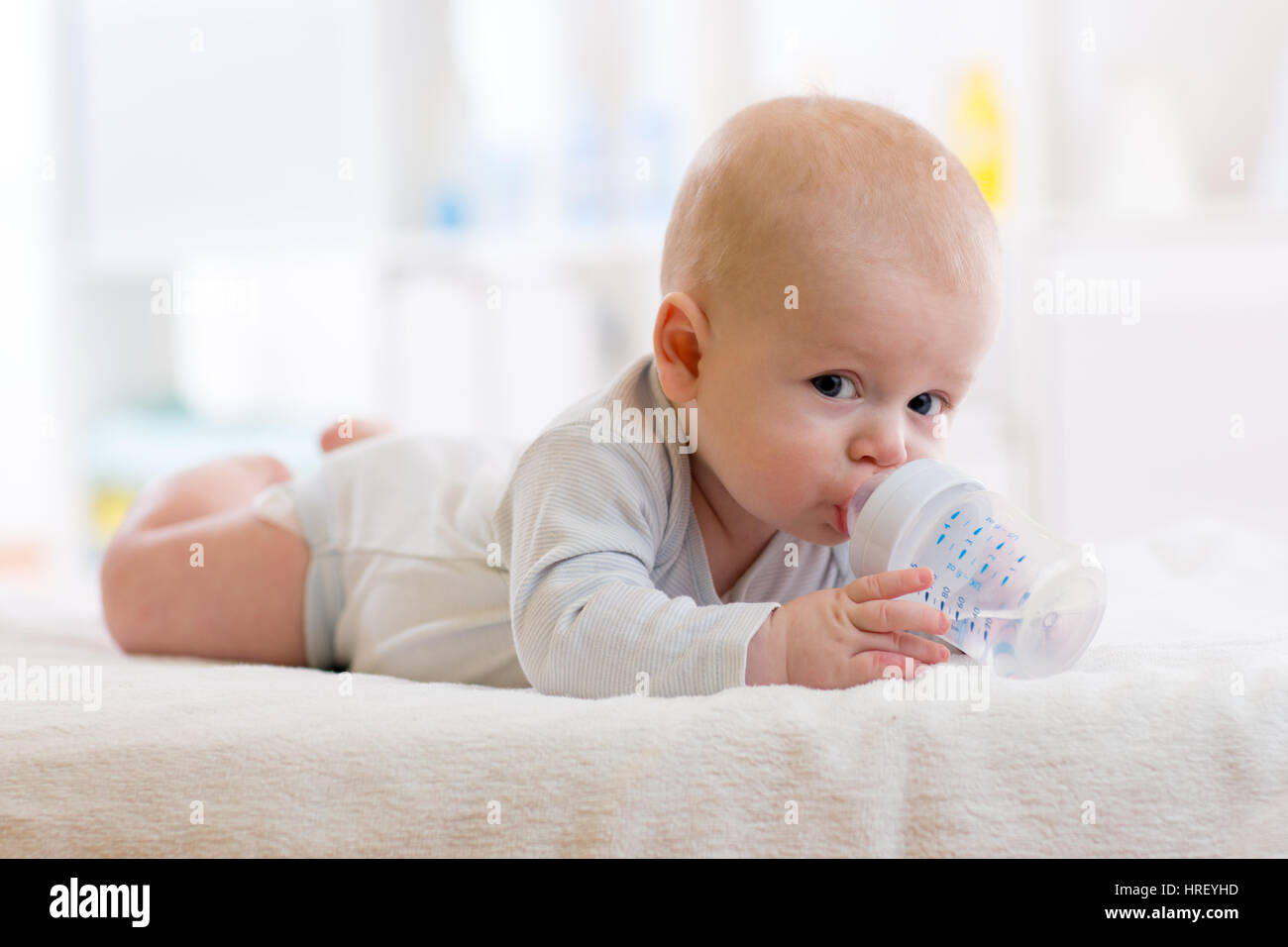 Sweet baby boy tenendo la bottiglia e acqua potabile in vivaio Foto Stock
