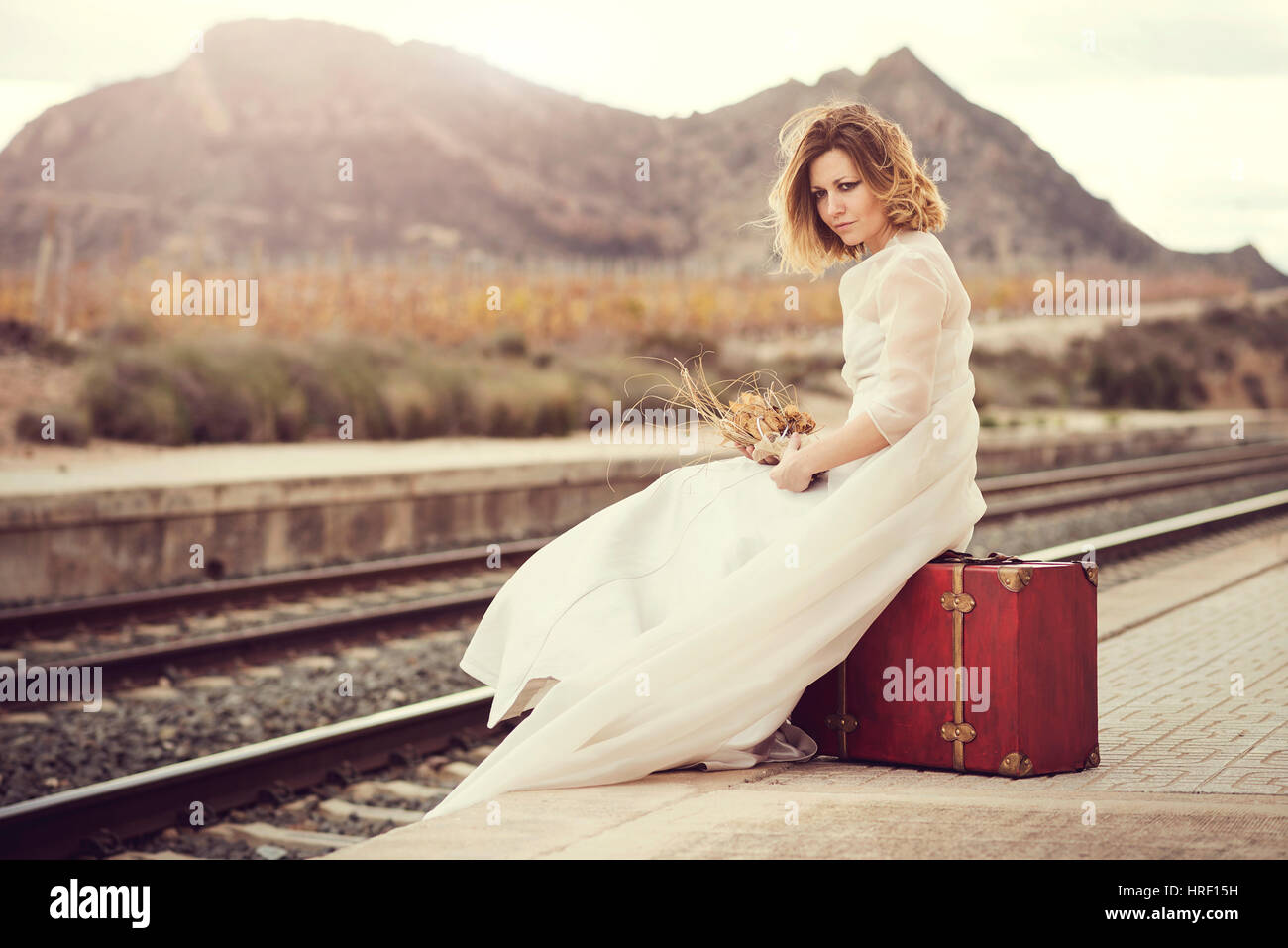 Malinconici sposa con una valigia rossa sui binari del treno Foto Stock