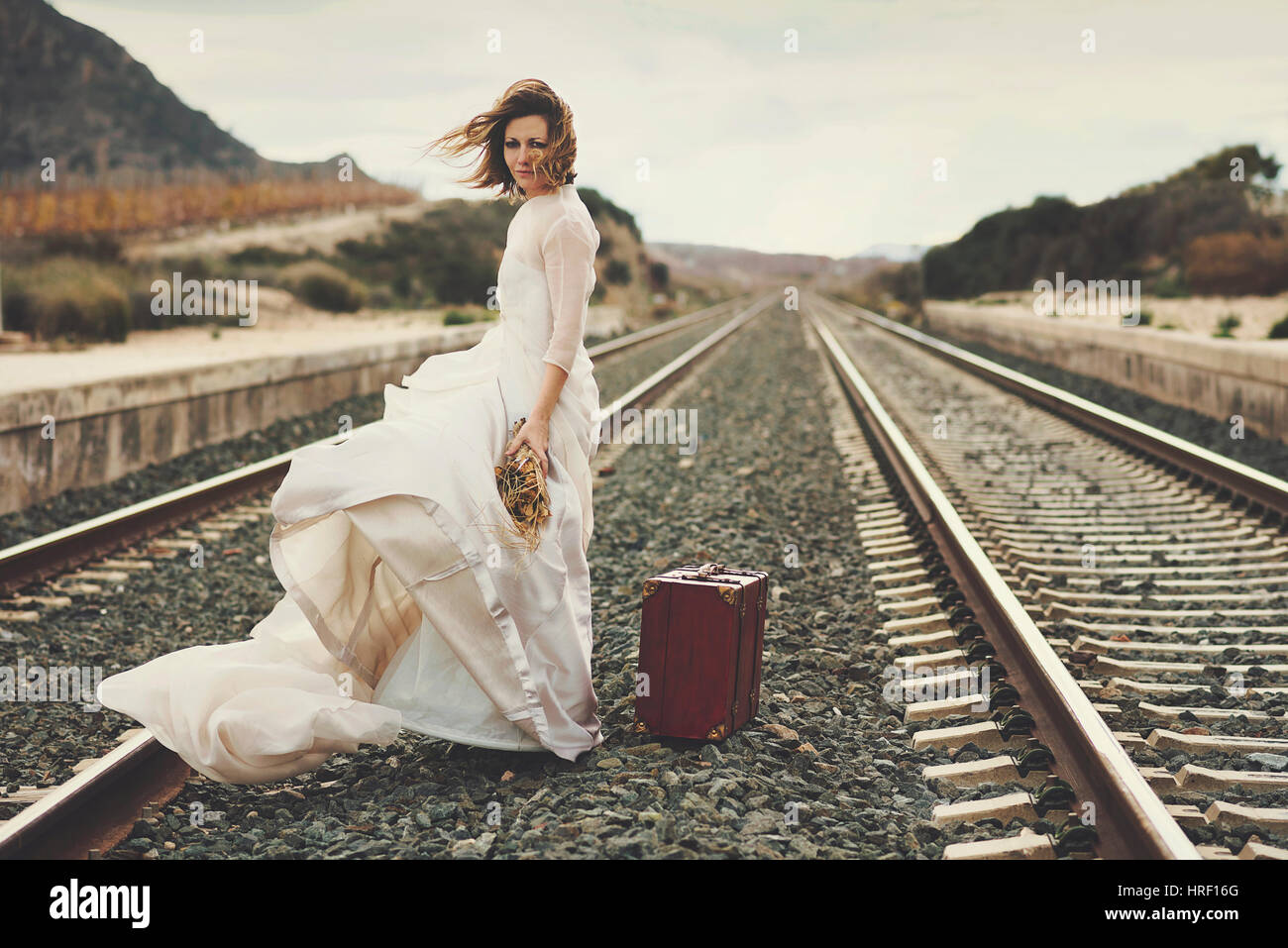 Malinconici sposa con una valigia rossa sui binari del treno Foto Stock