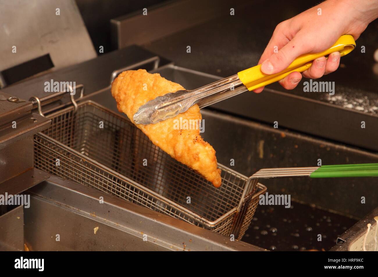 Sollevamento di un pezzo di travagliato cod al di fuori della friggitrice. Foto Stock