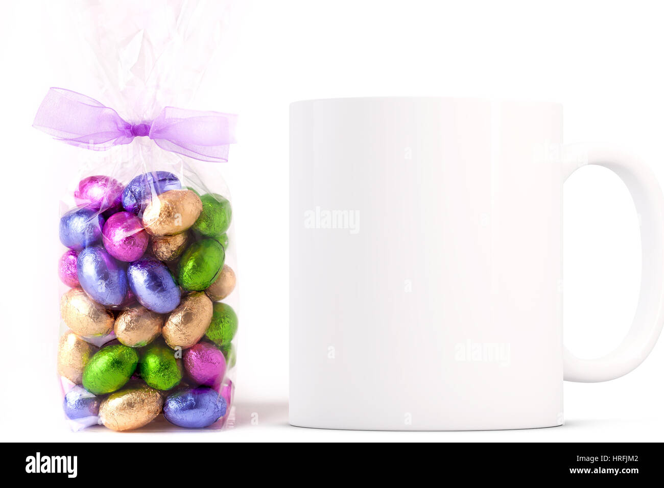 Pasqua tazza da caffè mockup accanto a un cellophane avvolto in borsa di oro cioccolato avvolto mini uova. Sovrapporre il proprio preventivi personalizzati e disegni per la vendita di tazze Foto Stock