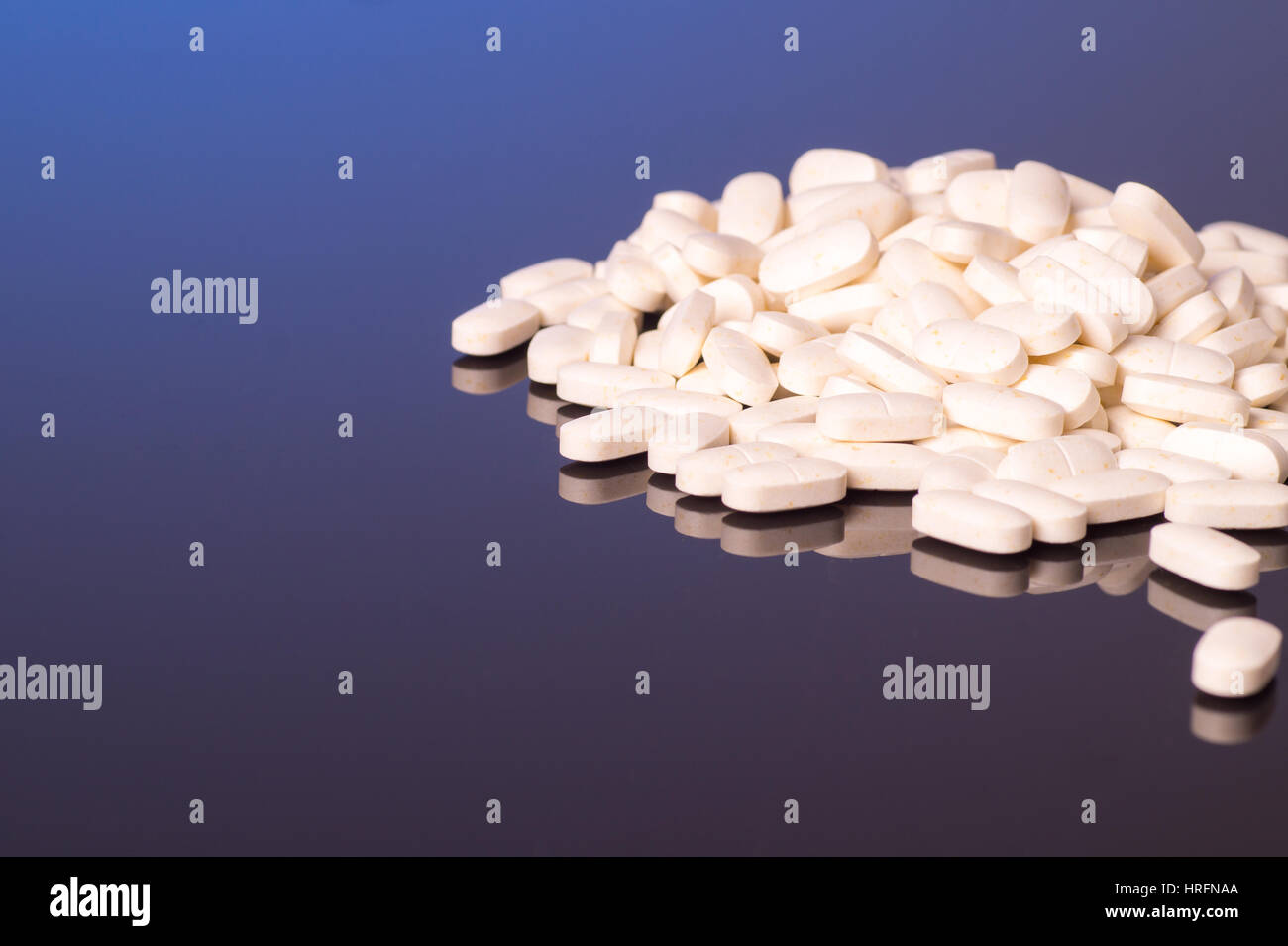 Un mucchio di pillole di bianco, è isolato su un lucido nero sfondo blu Foto Stock