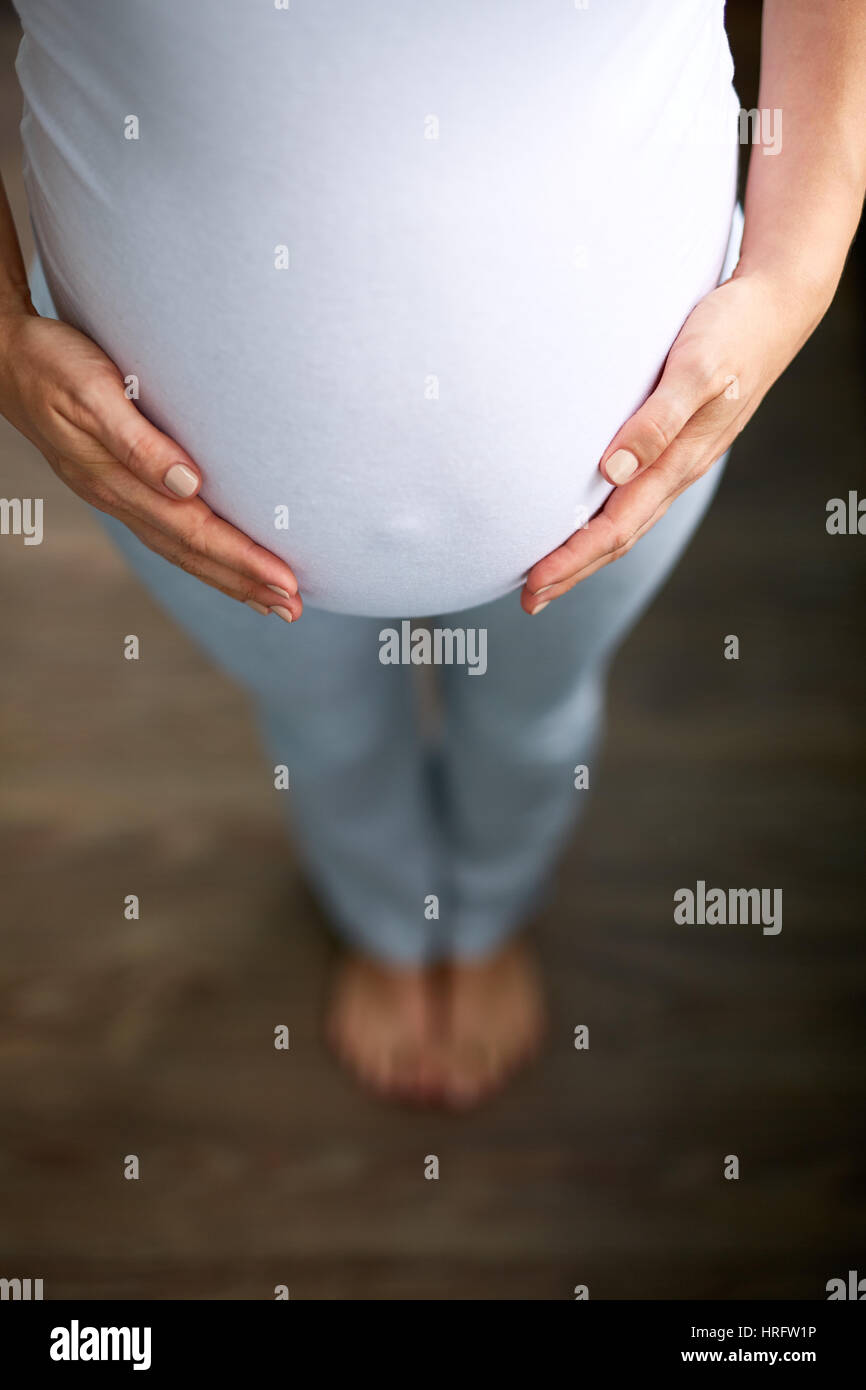 Guardando verso il basso immagine della donna incinta con pulsante di emergenza prendendo fuori attraverso la camicia Foto Stock