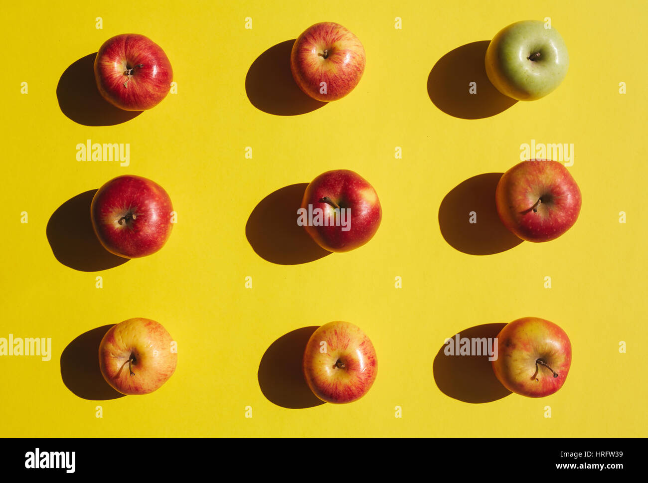 Direttamente sopra vista mature mele rosse disposte in righe, con una mela verde in piedi fuori, sul colore giallo brillante background, mangiare sano concetto Foto Stock