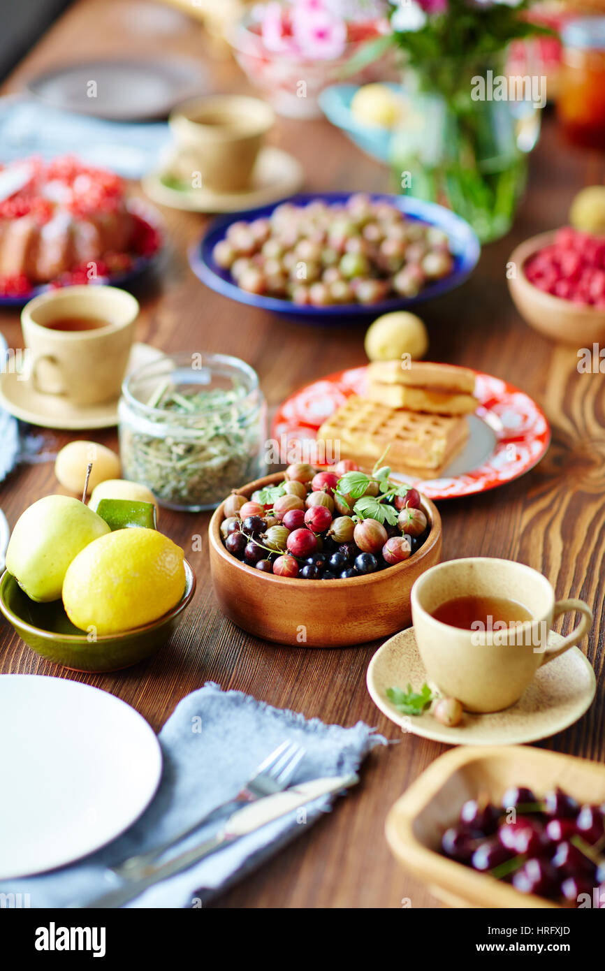 La colazione impostazione tabella piena di uva spina e ribes, frutta, pane appena sfornato, cialde e tazze di tè profumato Foto Stock