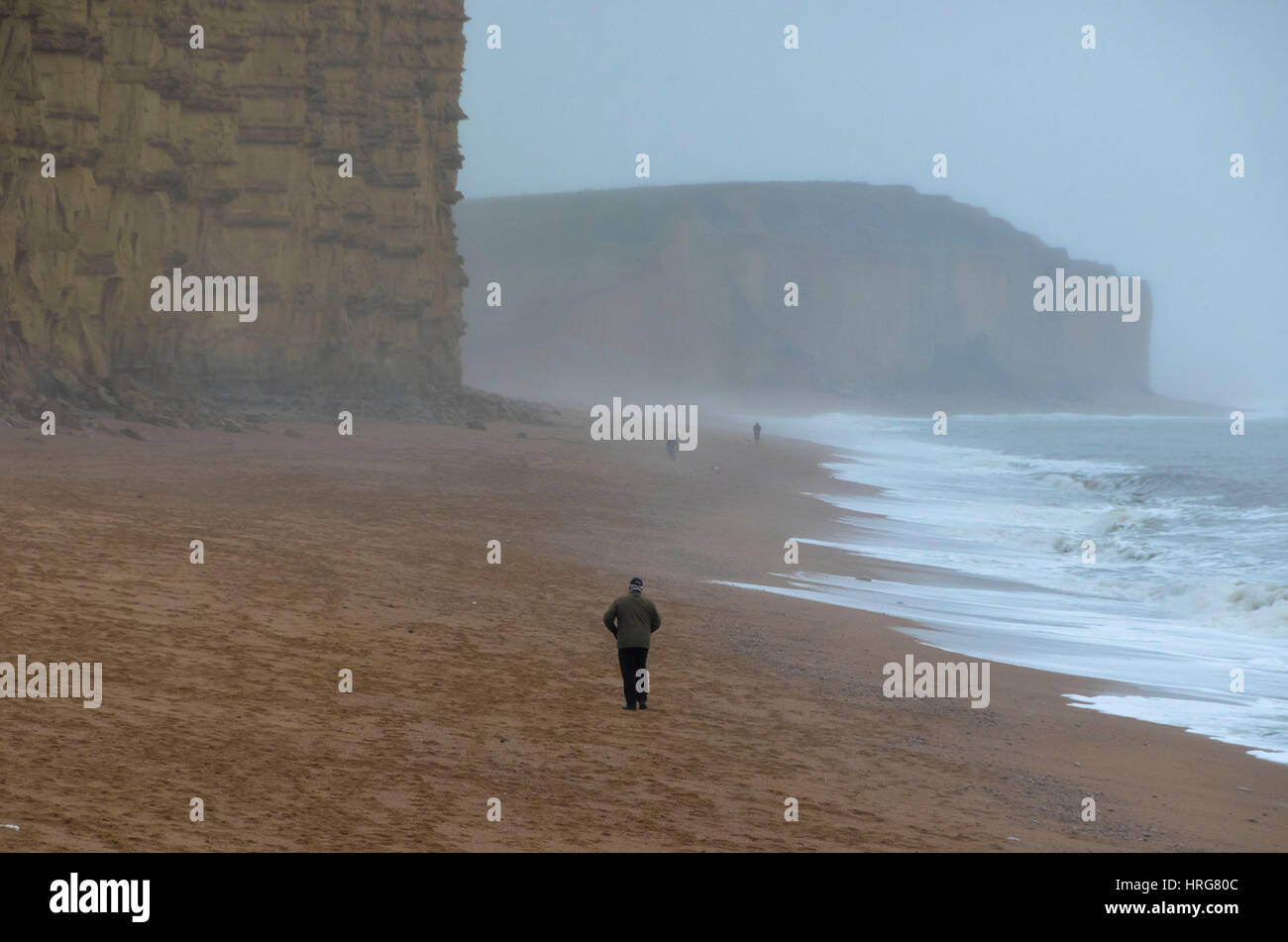 West Bay, Dorset, Regno Unito. 1 marzo 2017. Regno Unito Meteo. Un uomo a camminare sulla spiaggia a est su un drizzly nuvoloso giorno a West Bay nel Dorset il primo giorno di primavera meteorologica. Photo credit: Graham Hunt/Alamy Live News Foto Stock