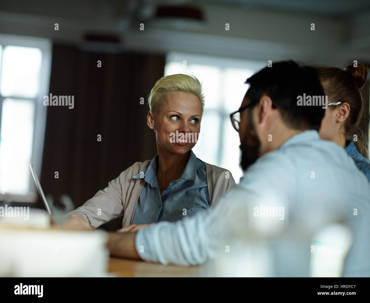 Ritratto di più moderno business persone vestite con abiti casual seduti insieme al tavolo nella sala dim, avente l'incontro per la discussione e la condivisione di idea Foto Stock
