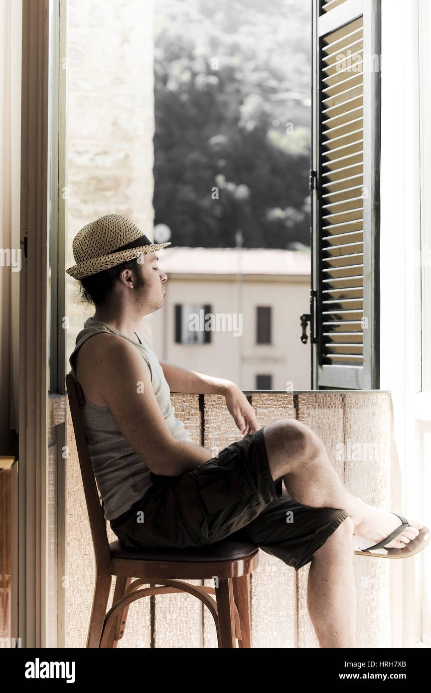 Modello rilasciato, Junger Mann mit Hut sitzt am offenen Fenster - l'uomo con il cappello accanto alla finestra Foto Stock