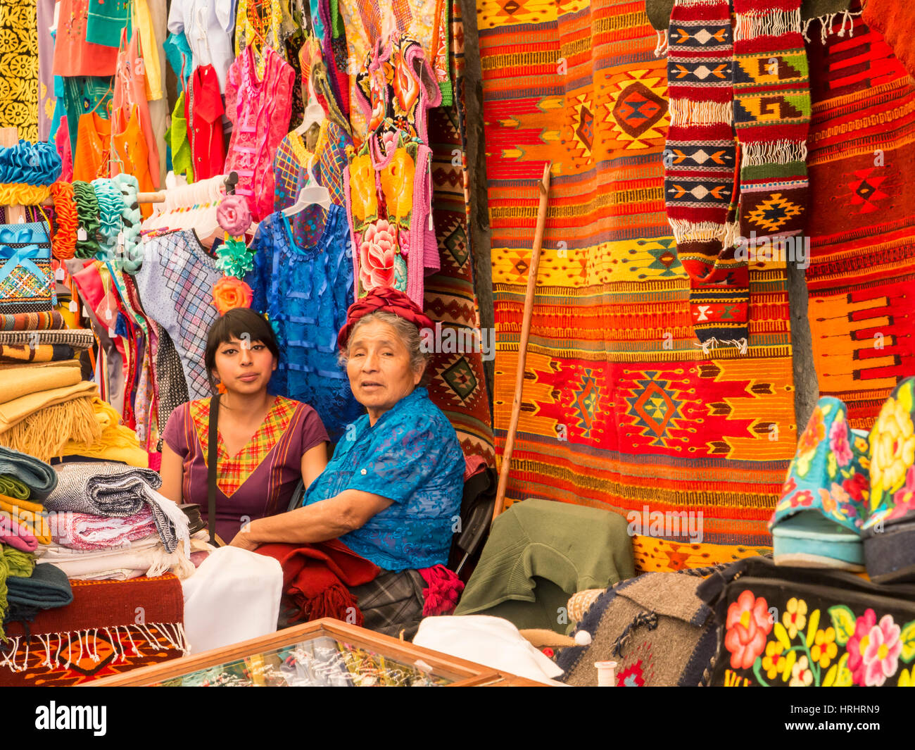 Le donne parlano in mercato con sfondo di tappeti fatti a mano e abbigliamento, Oaxaca, Messico, America del Nord Foto Stock