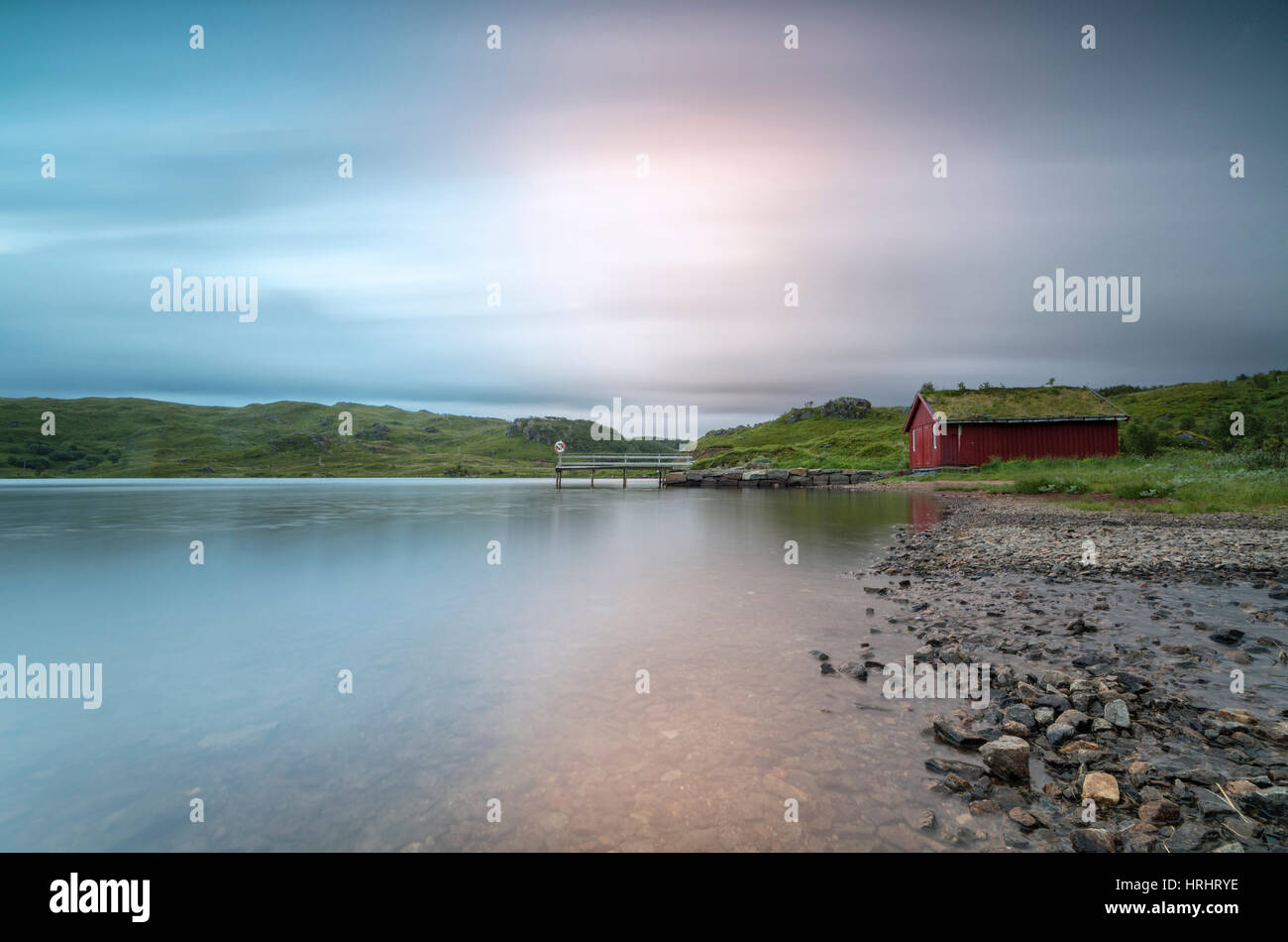 Luci rosa del sole di mezzanotte illuminare il mare e le tipiche rorbu, Holdalsvatnet, Vestvagoy, Isole Lofoten in Norvegia Foto Stock