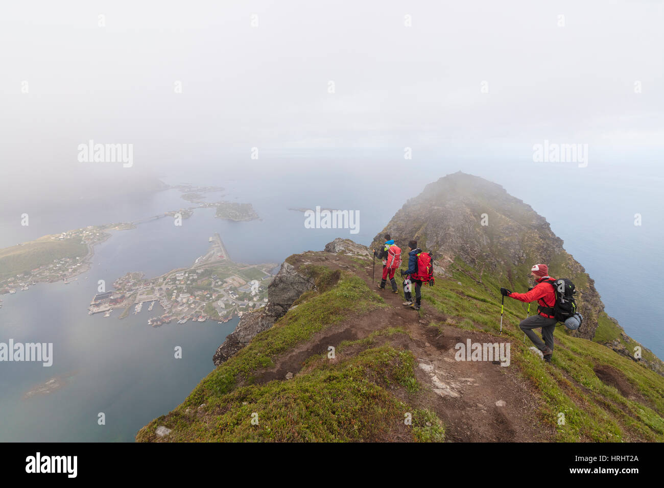 Gli escursionisti sulla sommità del picco roccioso ammirare il blu del mare circondato da nebbia, Reinebringen, Moskenesoya, Isole Lofoten in Norvegia Foto Stock