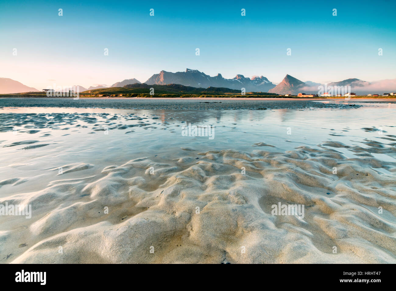 Picchi elevati e il sole di mezzanotte si riflettono nel mare freddo, Fredvang, Moskenesoya, Nordland county, Isole Lofoten in Norvegia Foto Stock