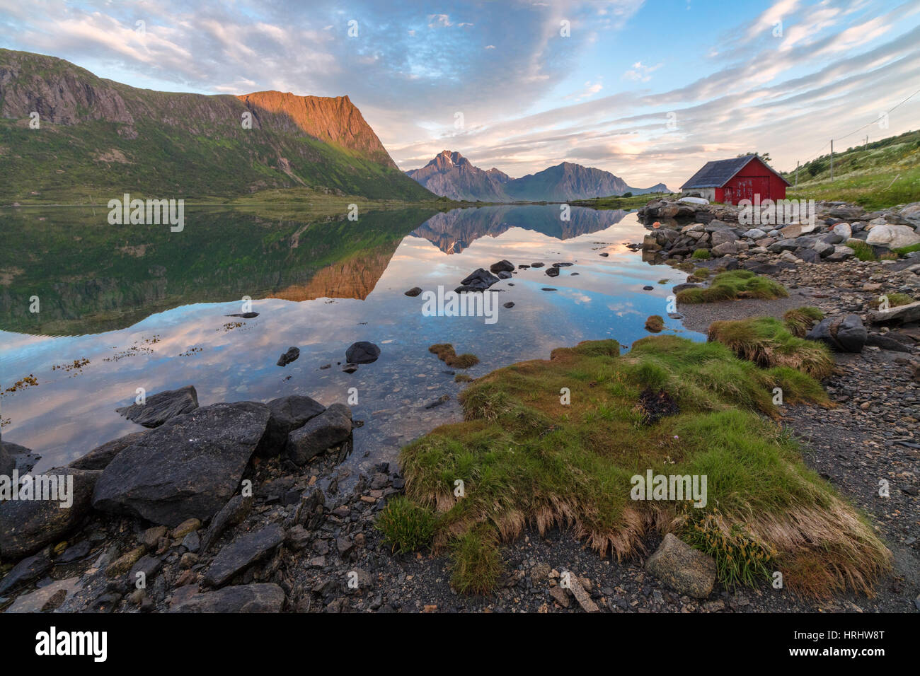 Nuvole rosa e picchi sono riflesse nel limpido mare di notte, Vengeren, Vagspollen, Isole Lofoten in Norvegia e Scandinavia Foto Stock