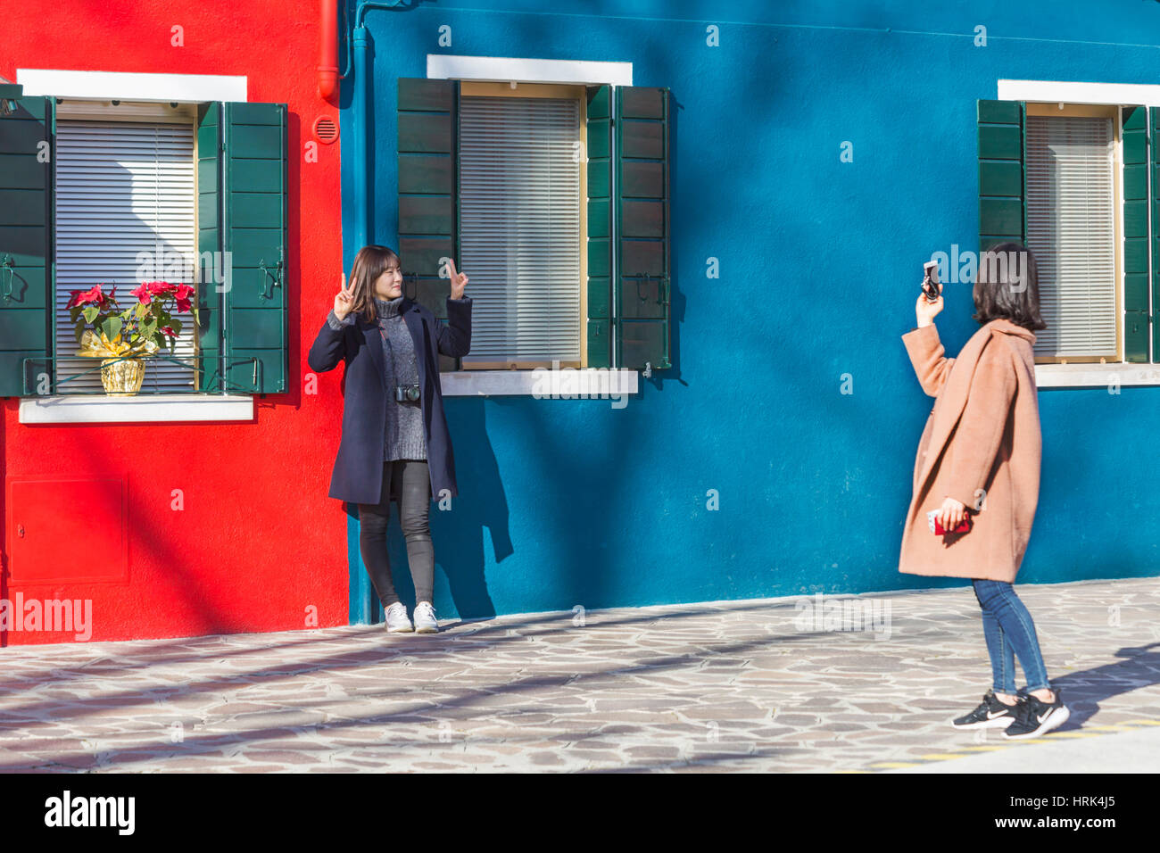 Turista femminile in posa per una fotografia di fronte blu luminoso e case rosso a Burano - colori luminosi di Burano Venezia Italia nel mese di gennaio Foto Stock