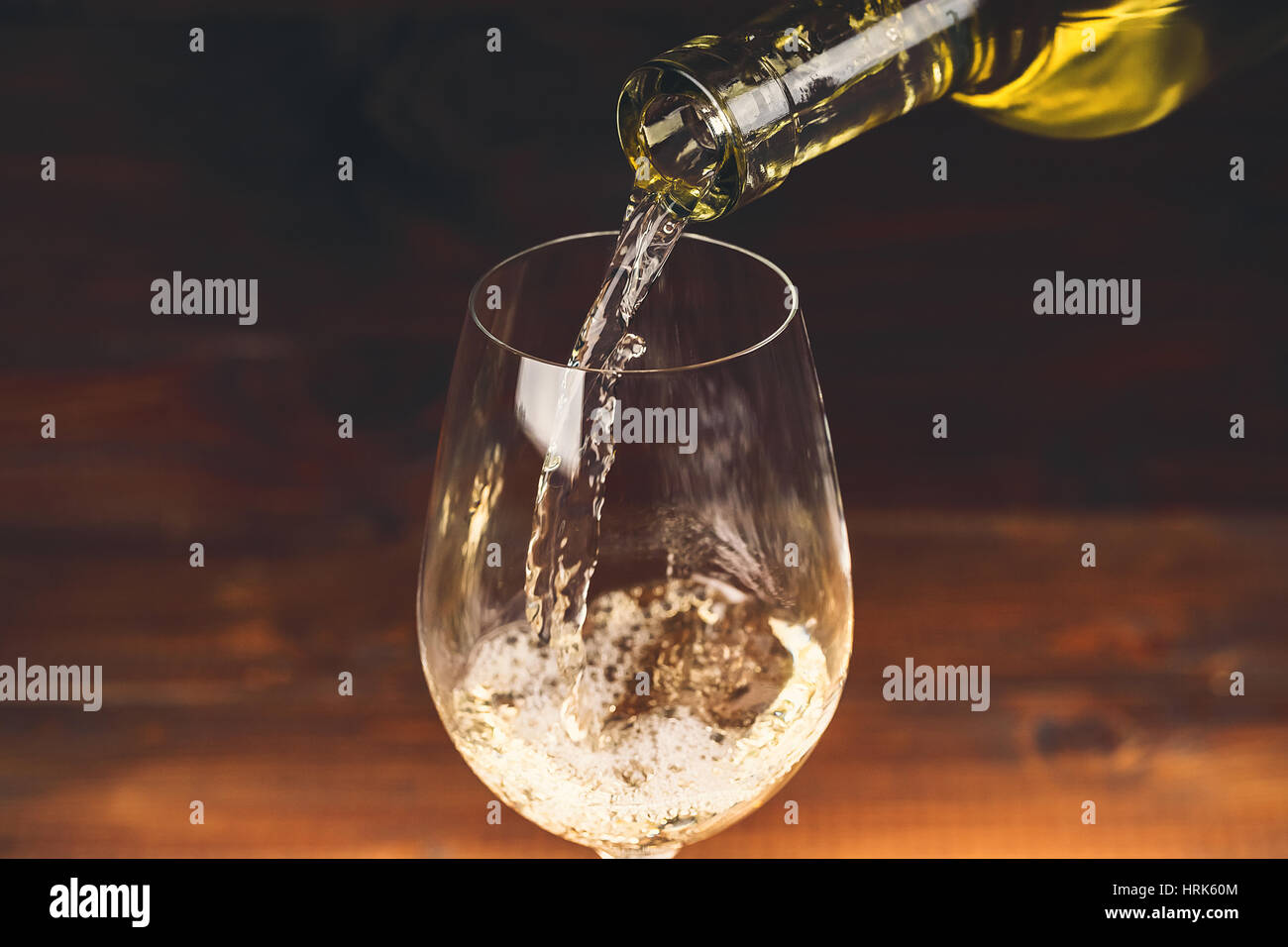 Versare il vino bianco da una bottiglia in un wineglasses su sfondo di legno. Spazio libero Foto Stock