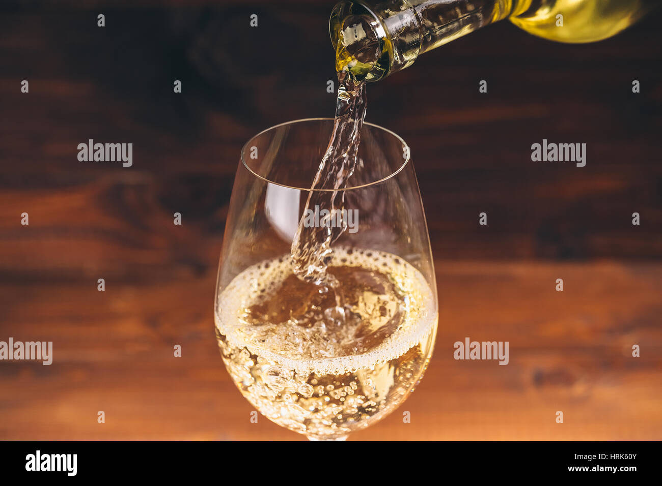 Versare il vino bianco da una bottiglia in un wineglasses su sfondo di legno. Spazio libero Foto Stock