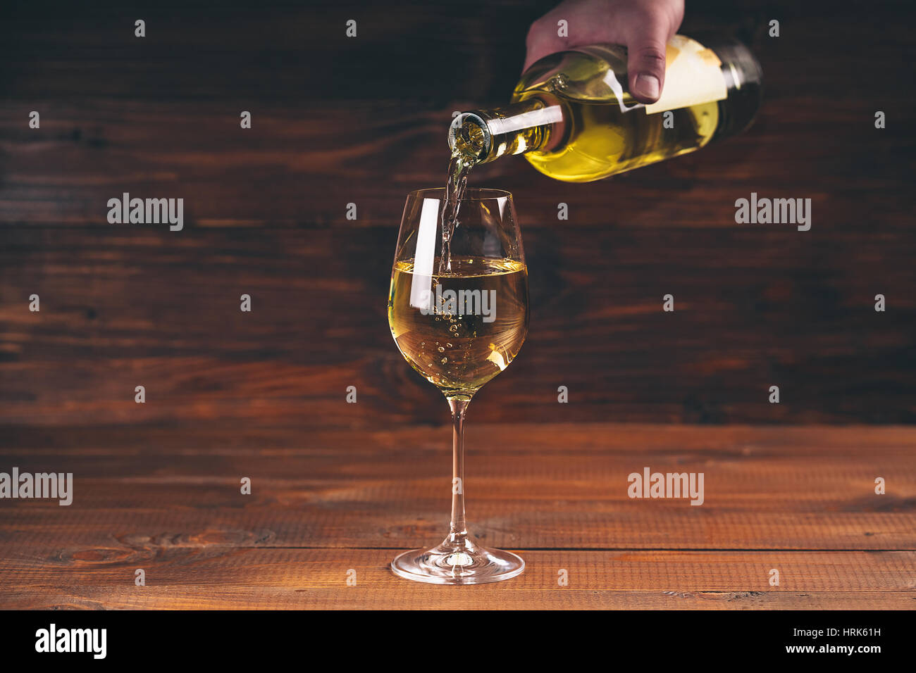 Versare il vino bianco da una bottiglia in una vista ravvicinata della wineglasses contro lo sfondo di legno Foto Stock