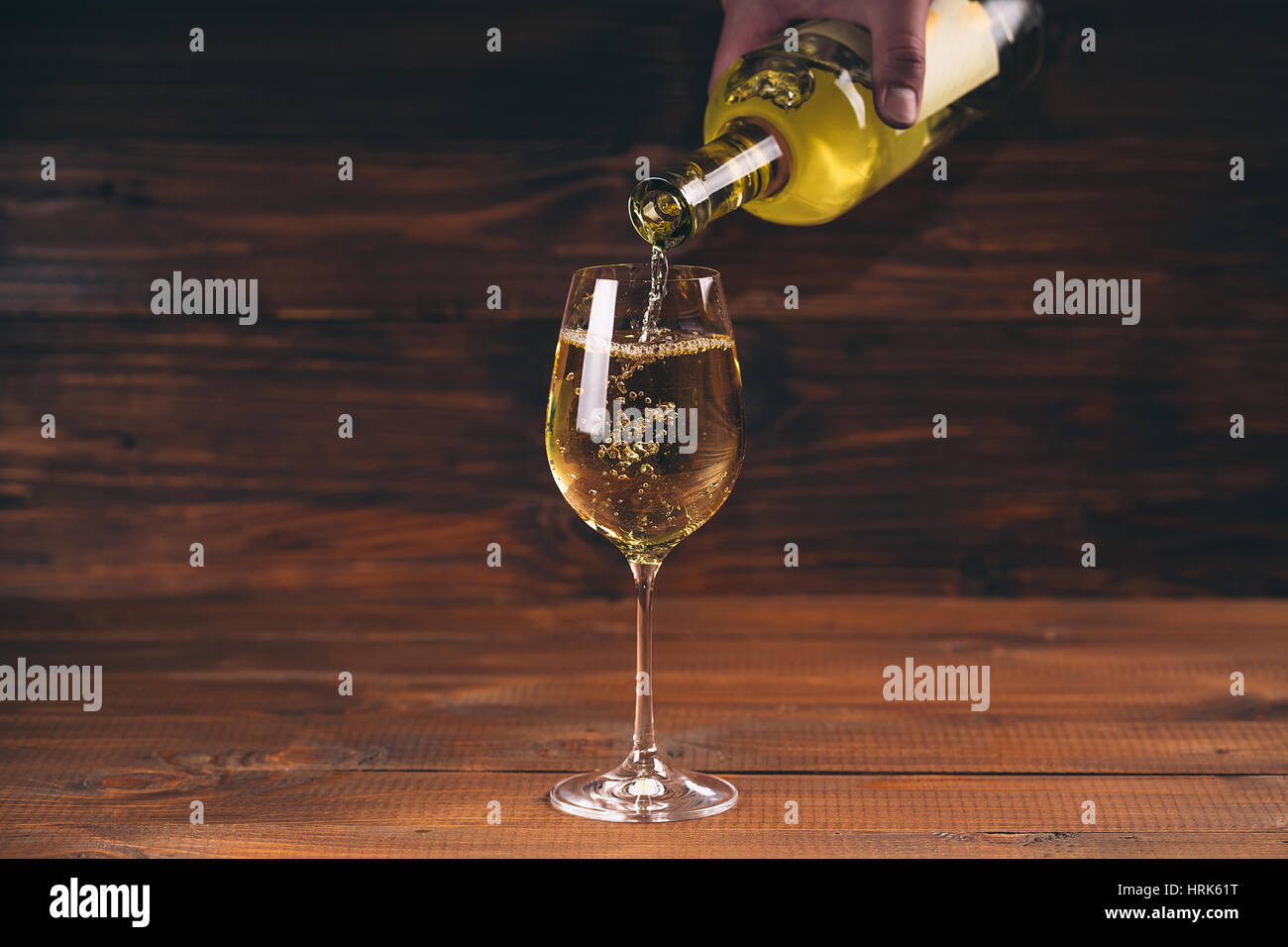 Versare il vino bianco da una bottiglia in un wineglasses su sfondo di legno. Spazio libero Foto Stock