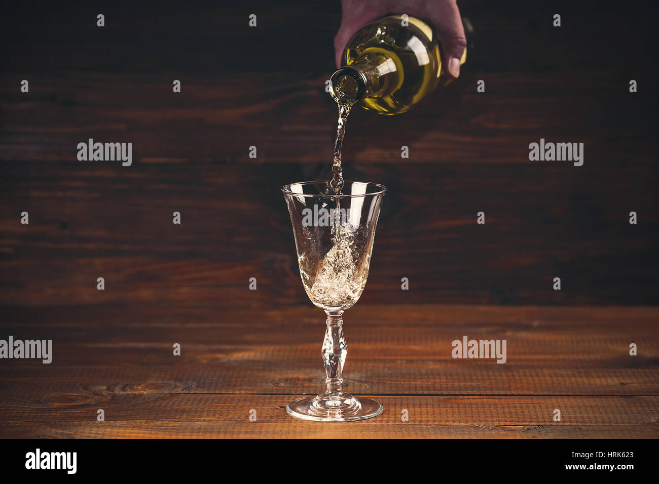 Versare il vino bianco da una bottiglia in un wineglasses su sfondo di legno. Spazio libero Foto Stock