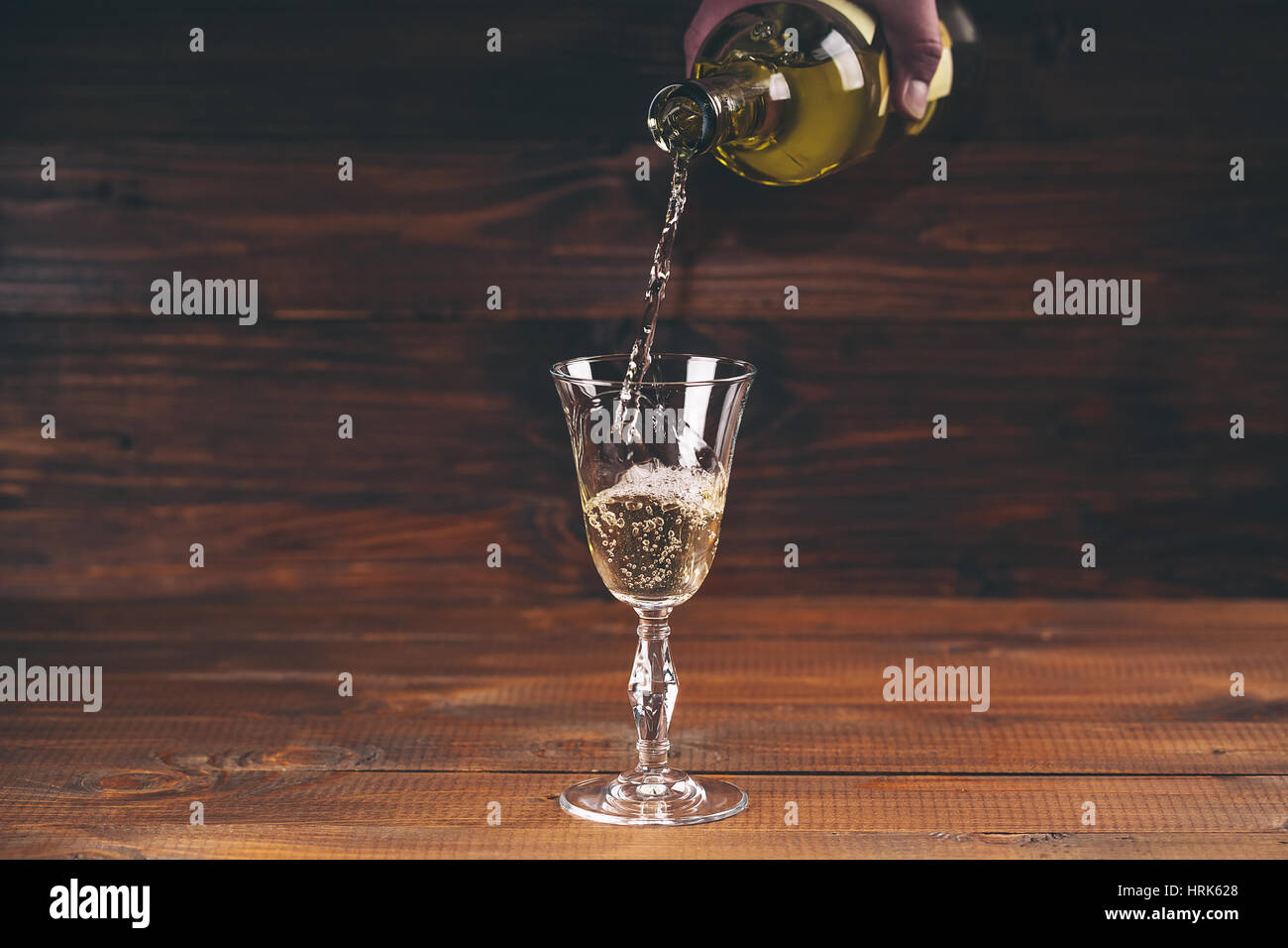 Versare il vino bianco da una bottiglia in un wineglasses su sfondo di legno. Spazio libero Foto Stock