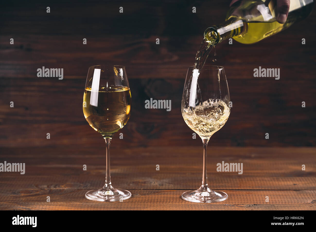 Due bicchieri versando il vino bianco da una bottiglia in un wineglass su sfondo di legno Foto Stock