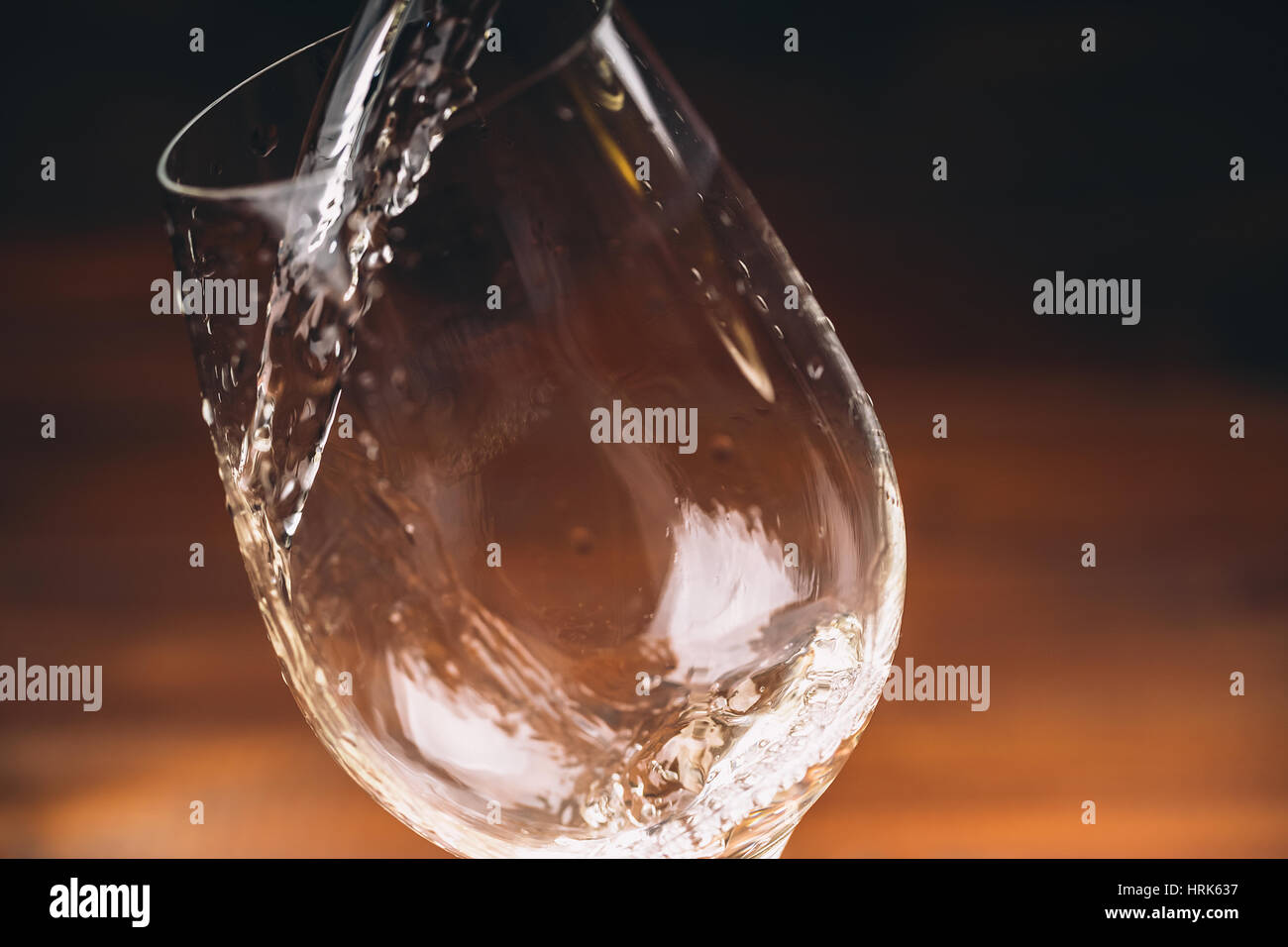 Versare il vino bianco da una bottiglia in una vista ravvicinata della wineglasses contro lo sfondo di legno Foto Stock