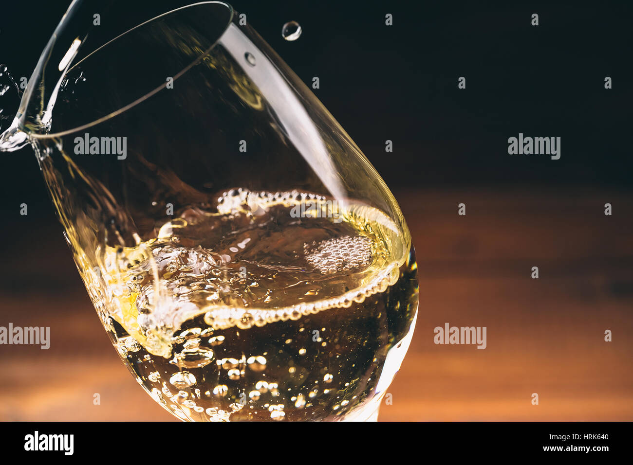 Versare il vino bianco da una bottiglia in un wineglasses su sfondo di legno. Spazio libero Foto Stock